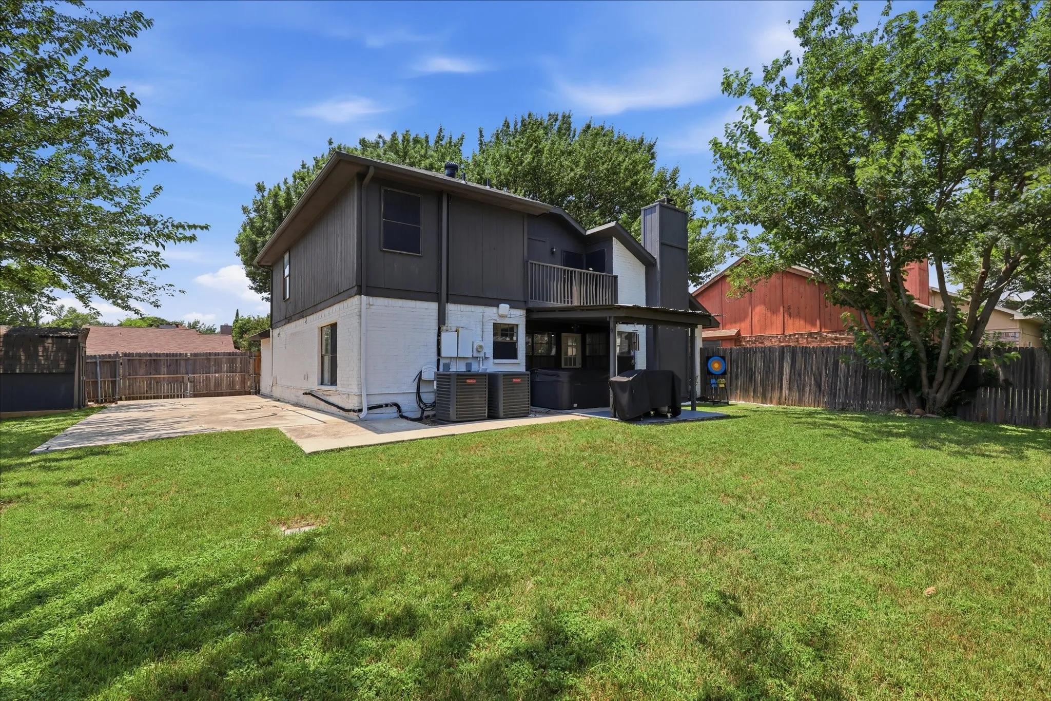 Expansive rear yard with a concrete patio, wood fence, and mature trees