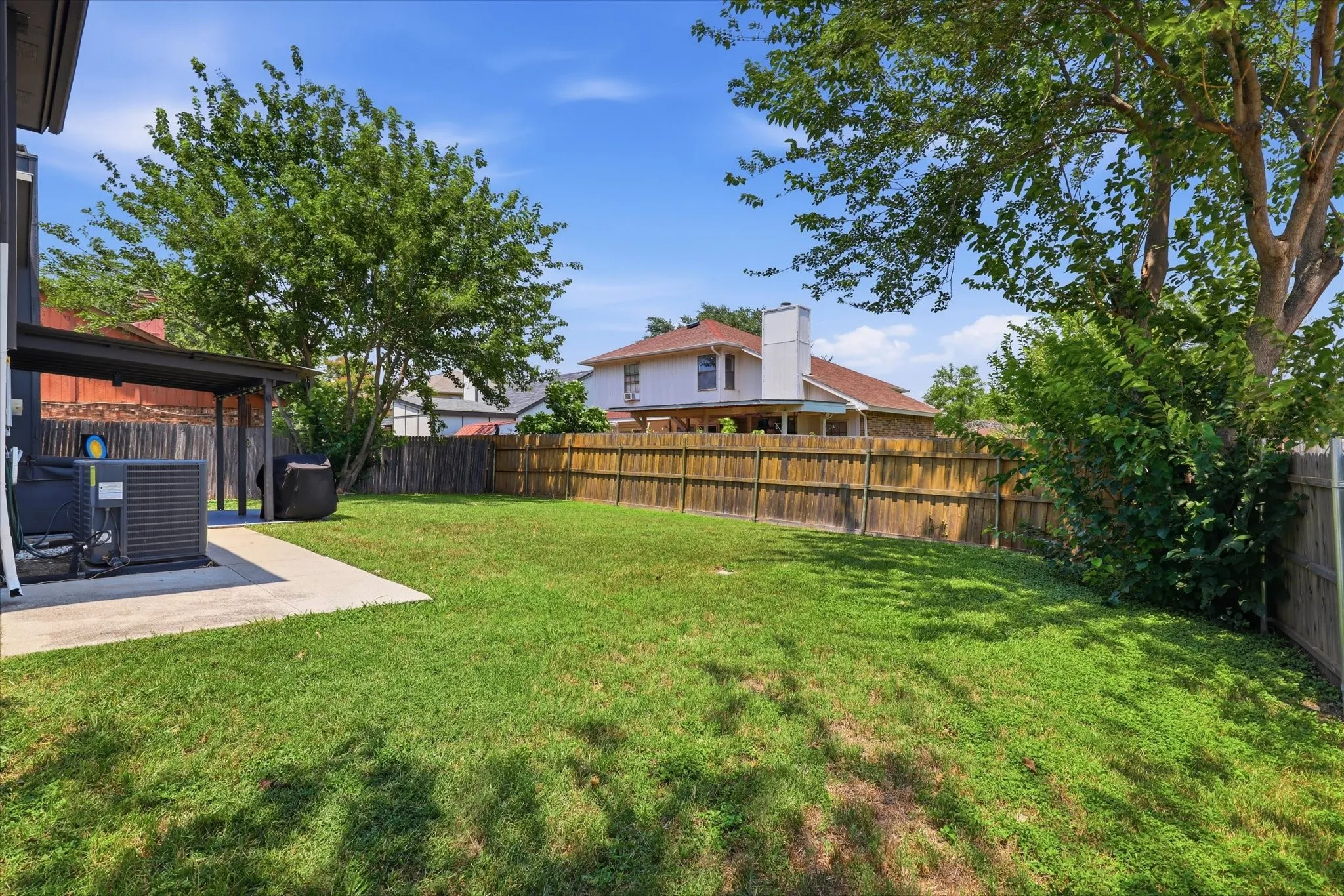 Expansive backyard featuring a manicured lawn, established trees, privacy fencing, and a concrete patio with an overhead awning