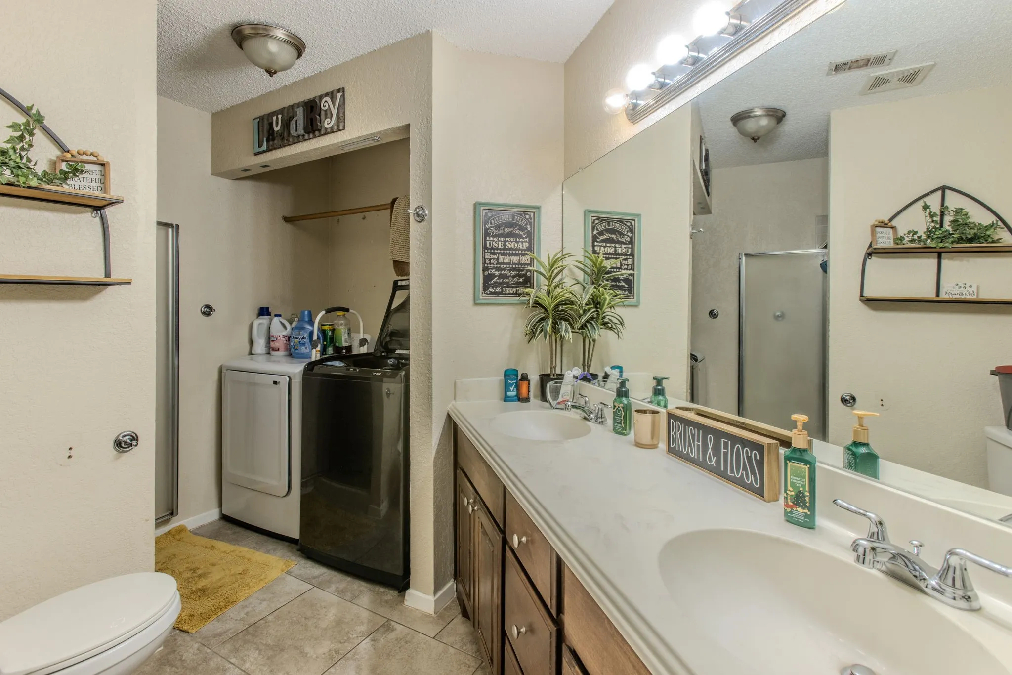 Dual vanity with integrated sinks, full-width mirror, tile flooring, and dedicated laundry area