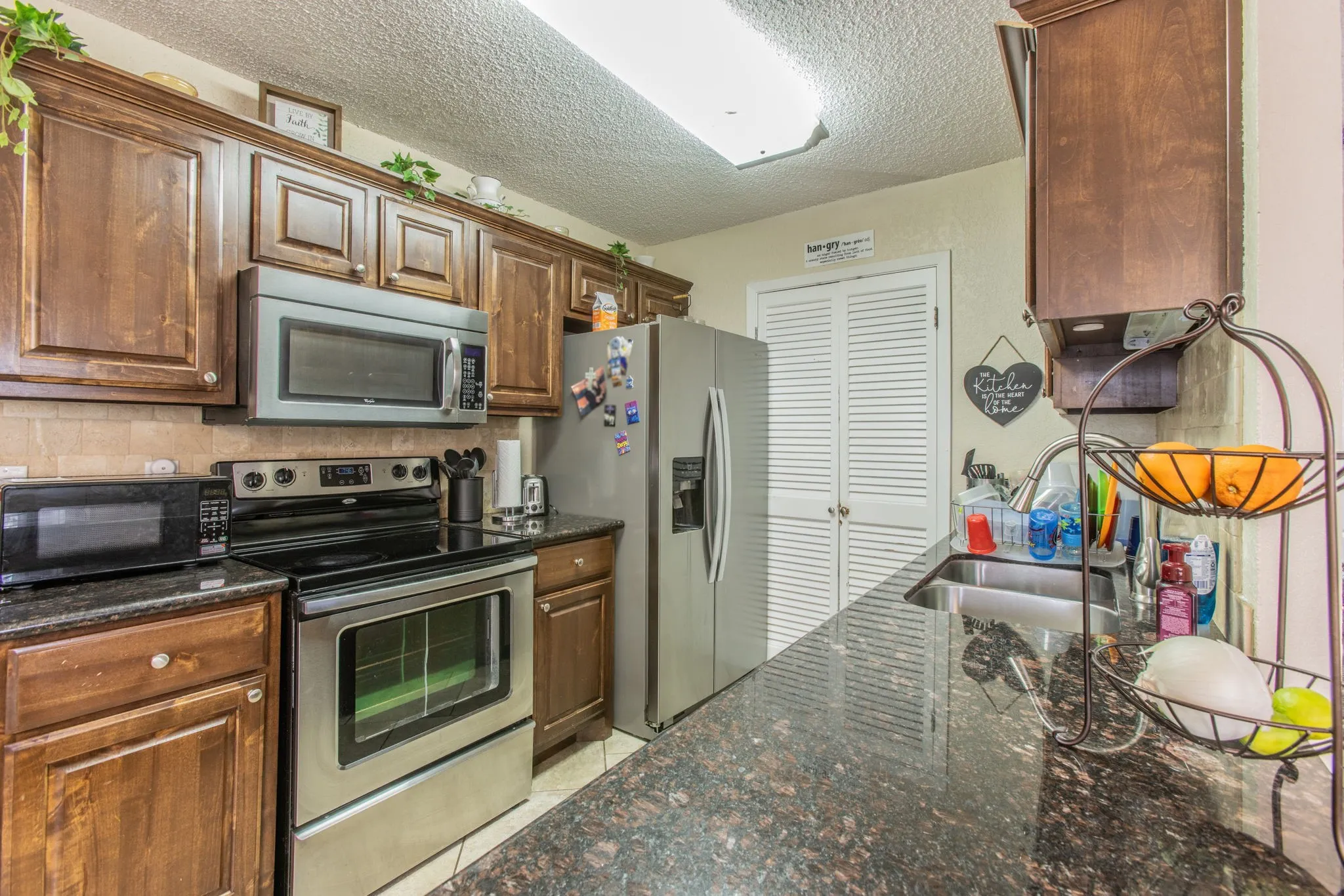 Kitchen featuring dark wood-finish cabinetry, stainless steel appliances, stone-finish countertops, and a tile backsplash