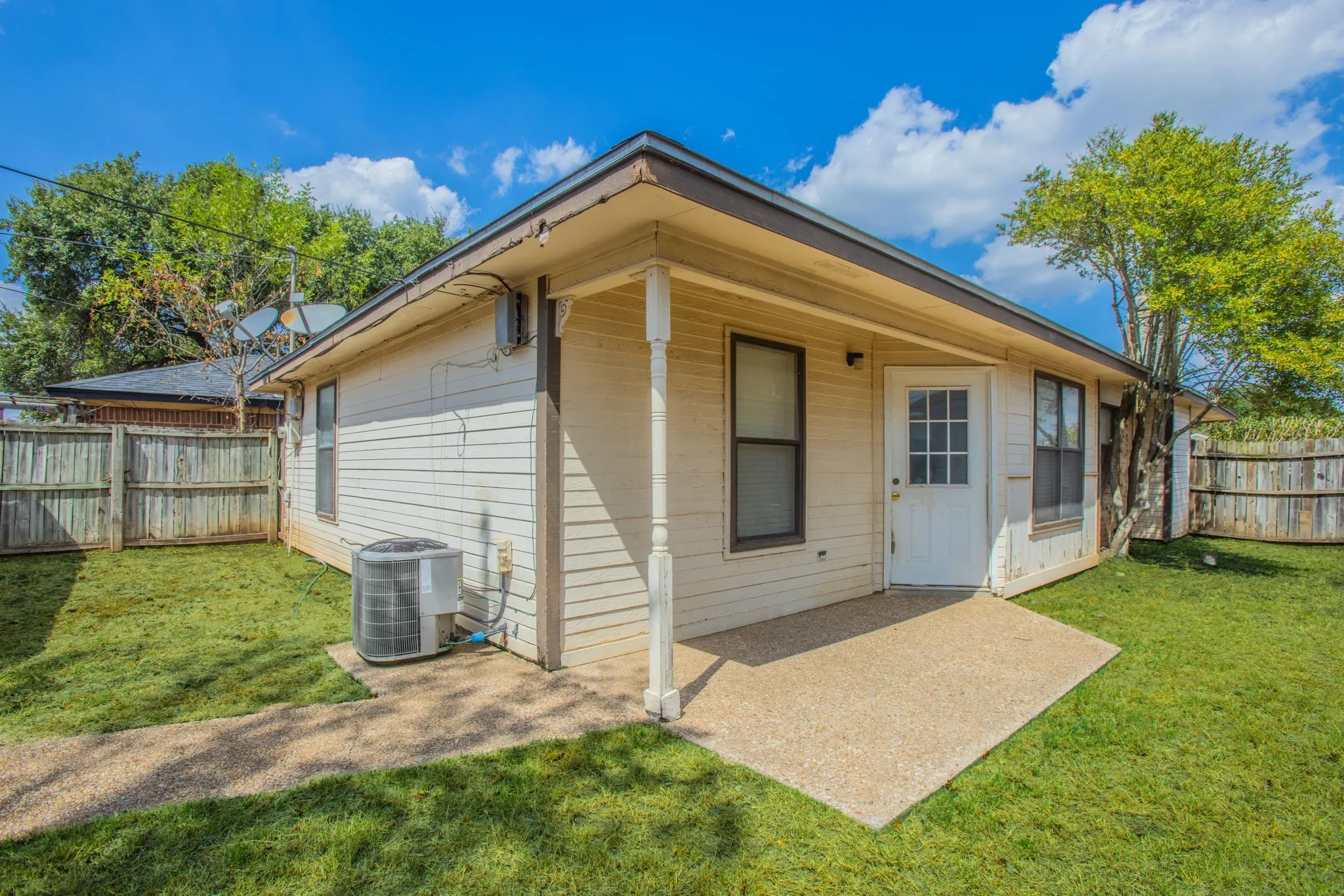 Exterior featuring siding, a small concrete patio, a white door with lites, and a fenced yard
