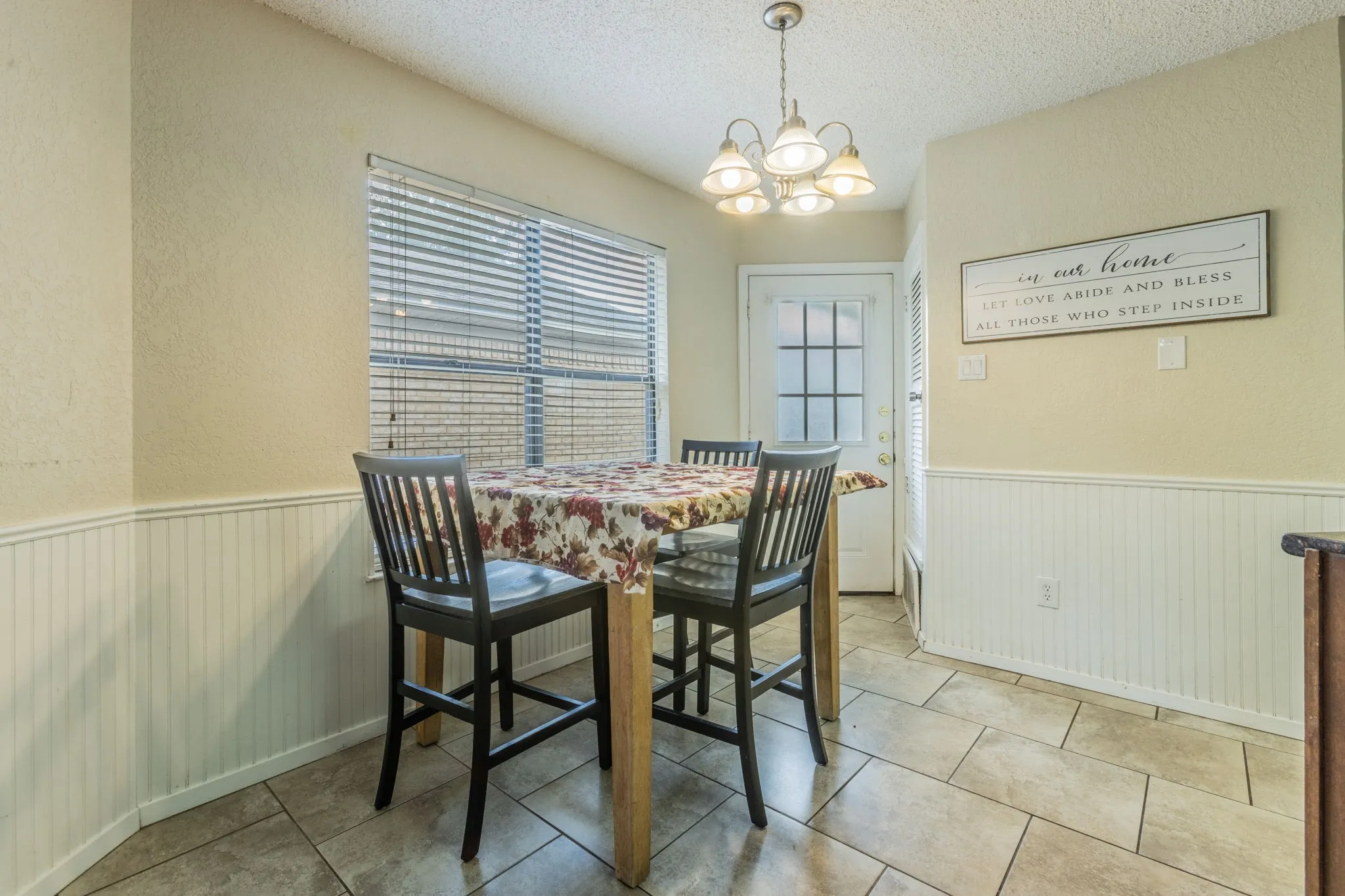 Tile flooring, beadboard wainscoting, window with blinds, paneled door with glass inserts, and a chandelier lighting fixture