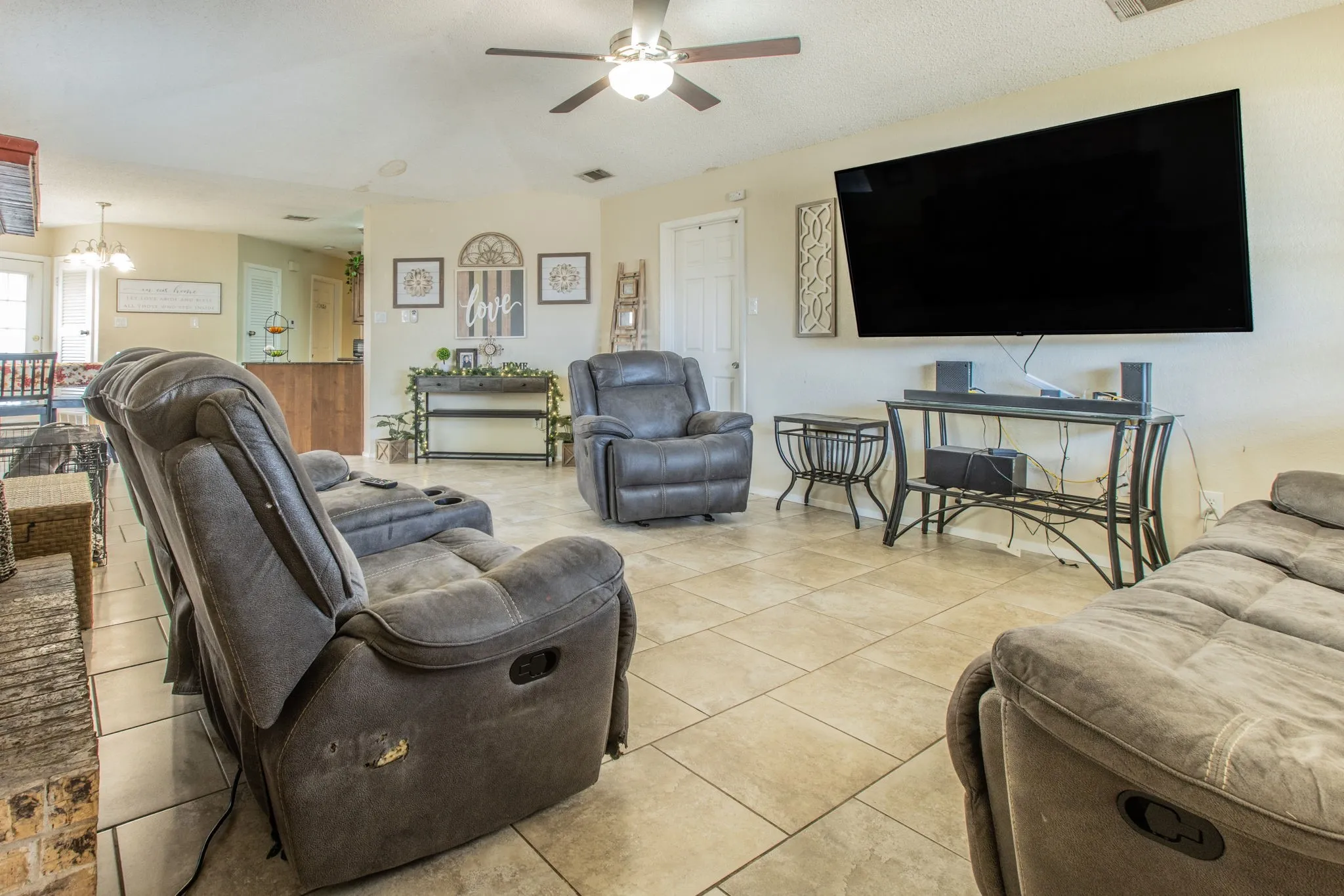 Spacious living area featuring neutral-toned tile flooring, a ceiling fan with integrated lighting, and light-colored wall paint
