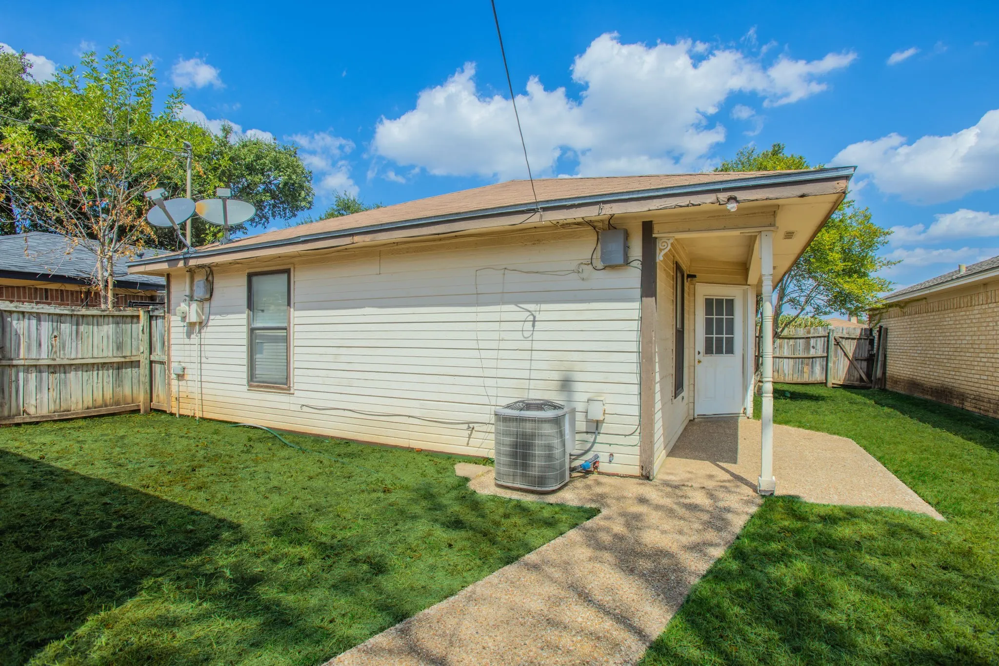 Expansive backyard featuring a manicured lawn, wood fencing, and a concrete patio with covered entry