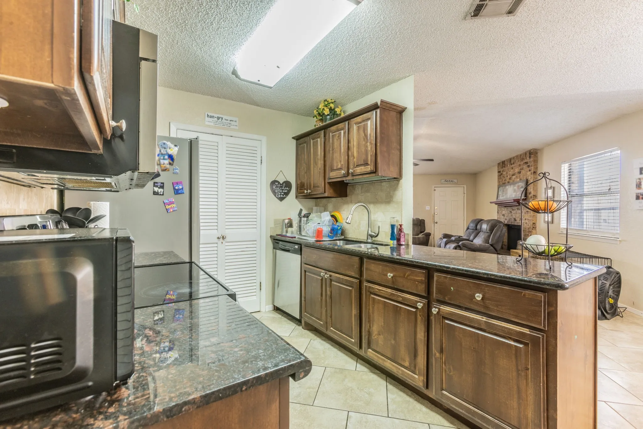 Kitchen featuring wood cabinetry, dark countertops, built-in stainless steel dishwasher, and tile flooring