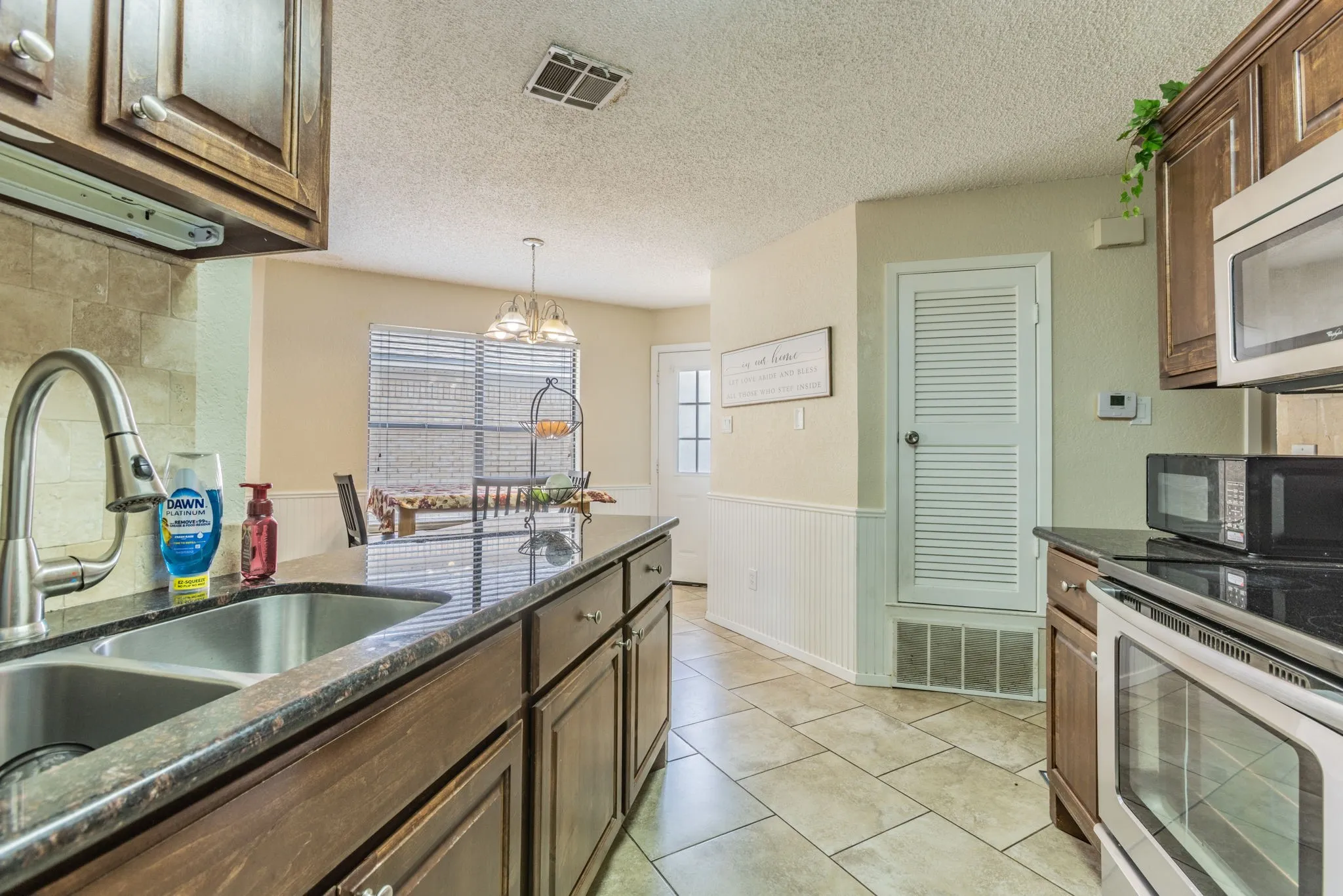 Kitchen featuring granite-look countertops, wood cabinetry, a dual basin stainless steel sink with a gooseneck faucet, and tile flooring