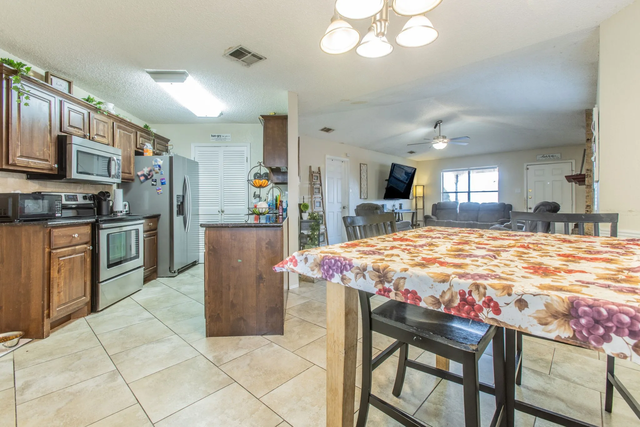 Tile flooring, wood-finish cabinetry, stainless steel appliances, breakfast bar, and ceiling fan