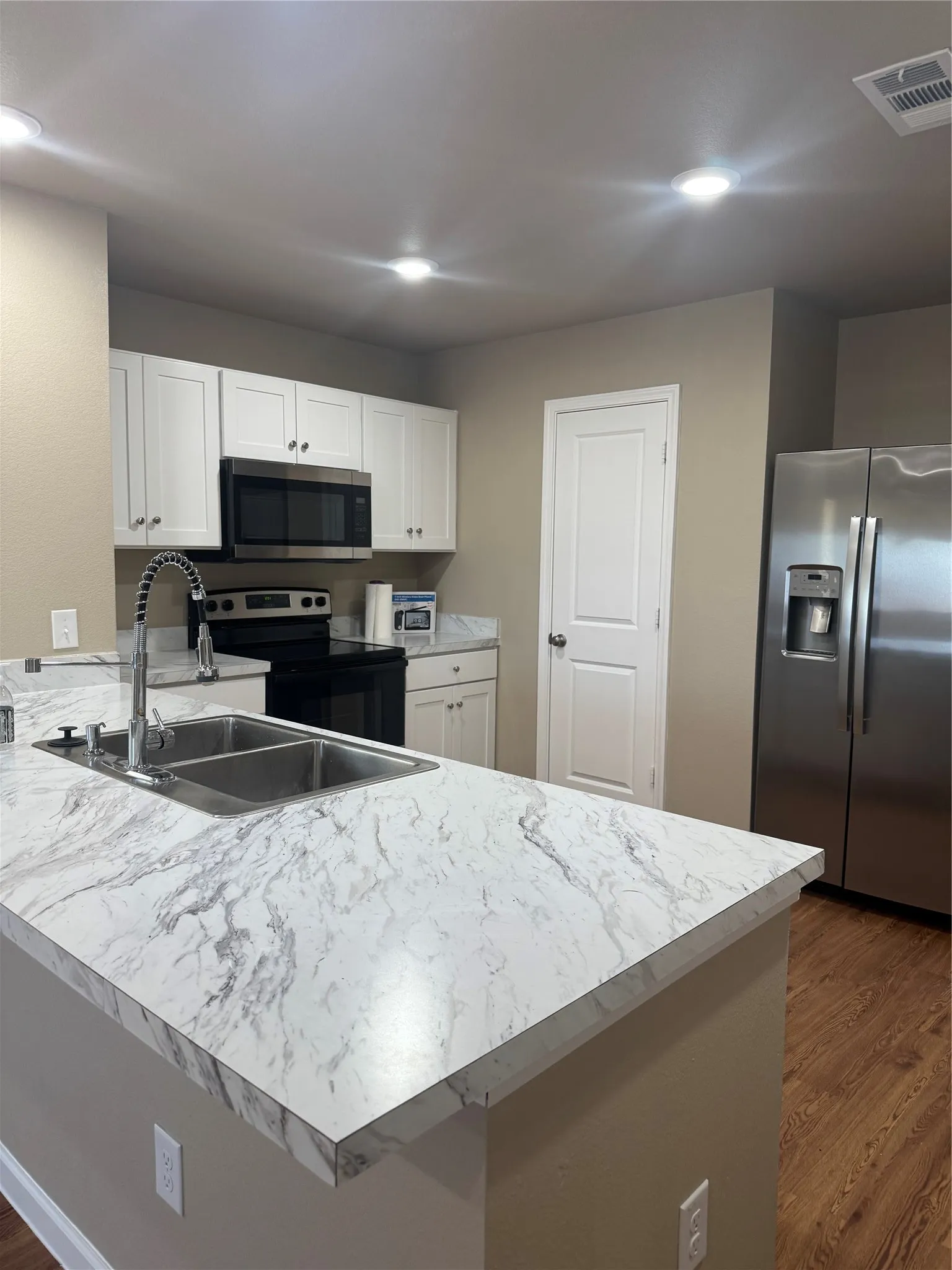 Kitchen featuring white shaker cabinetry, stainless steel appliances, a double basin sink with a high-arc faucet, wood-finish flooring, and recessed lighting