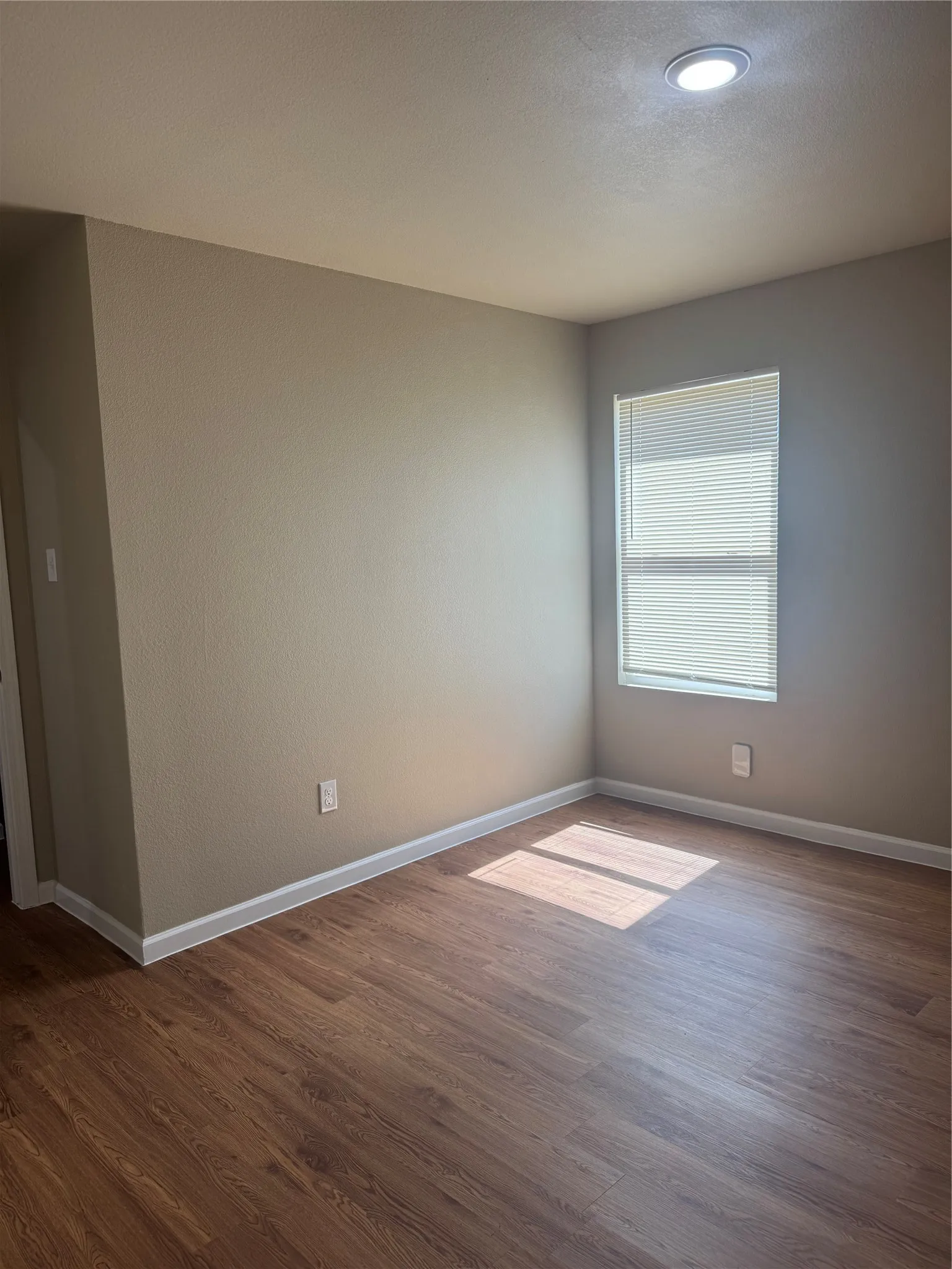 Recessed ceiling lighting, a window with blinds, and wood-finish flooring
