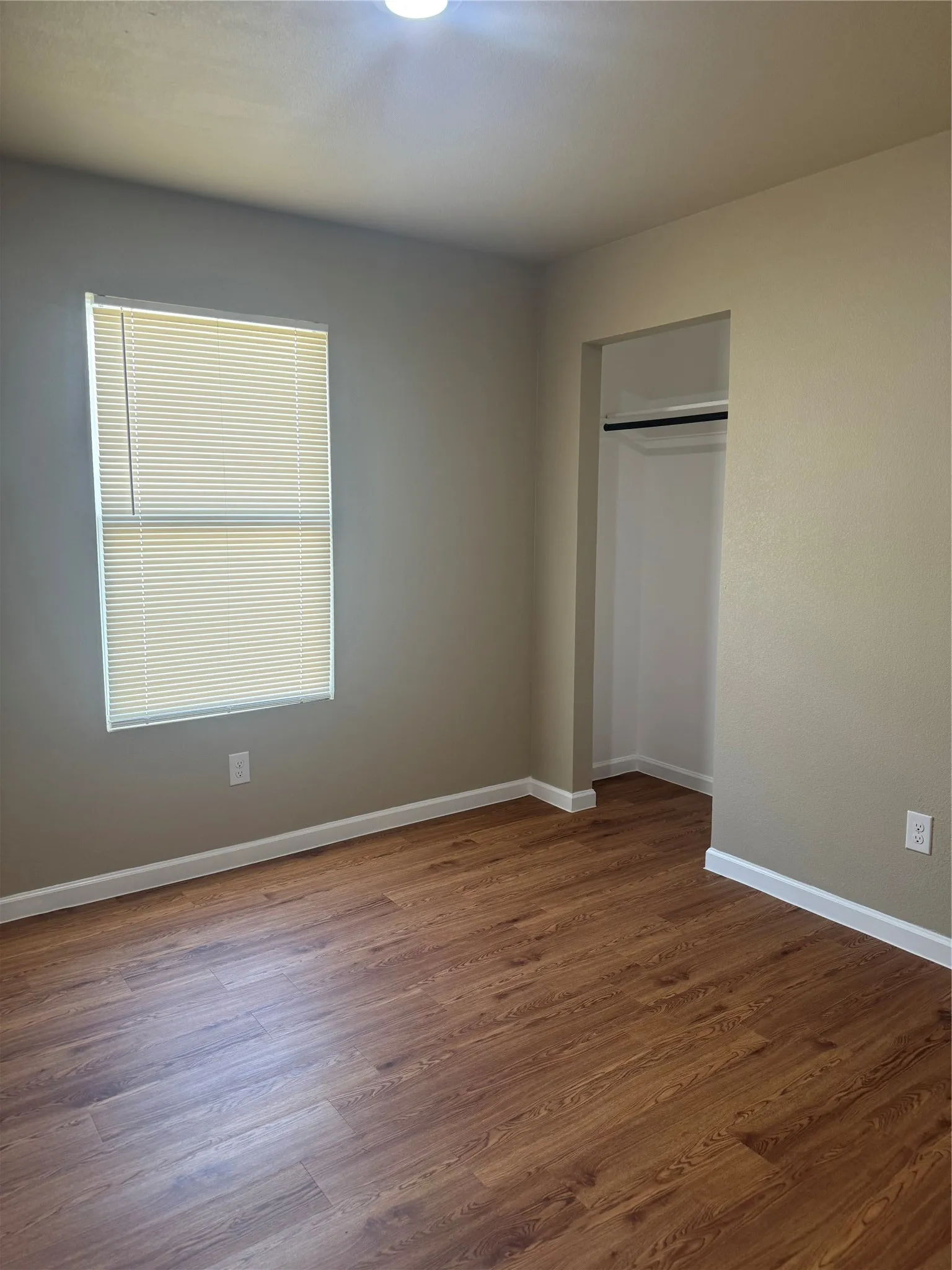 Wood-finish flooring, recessed lighting, window with blinds, and an open closet with hanging rod
