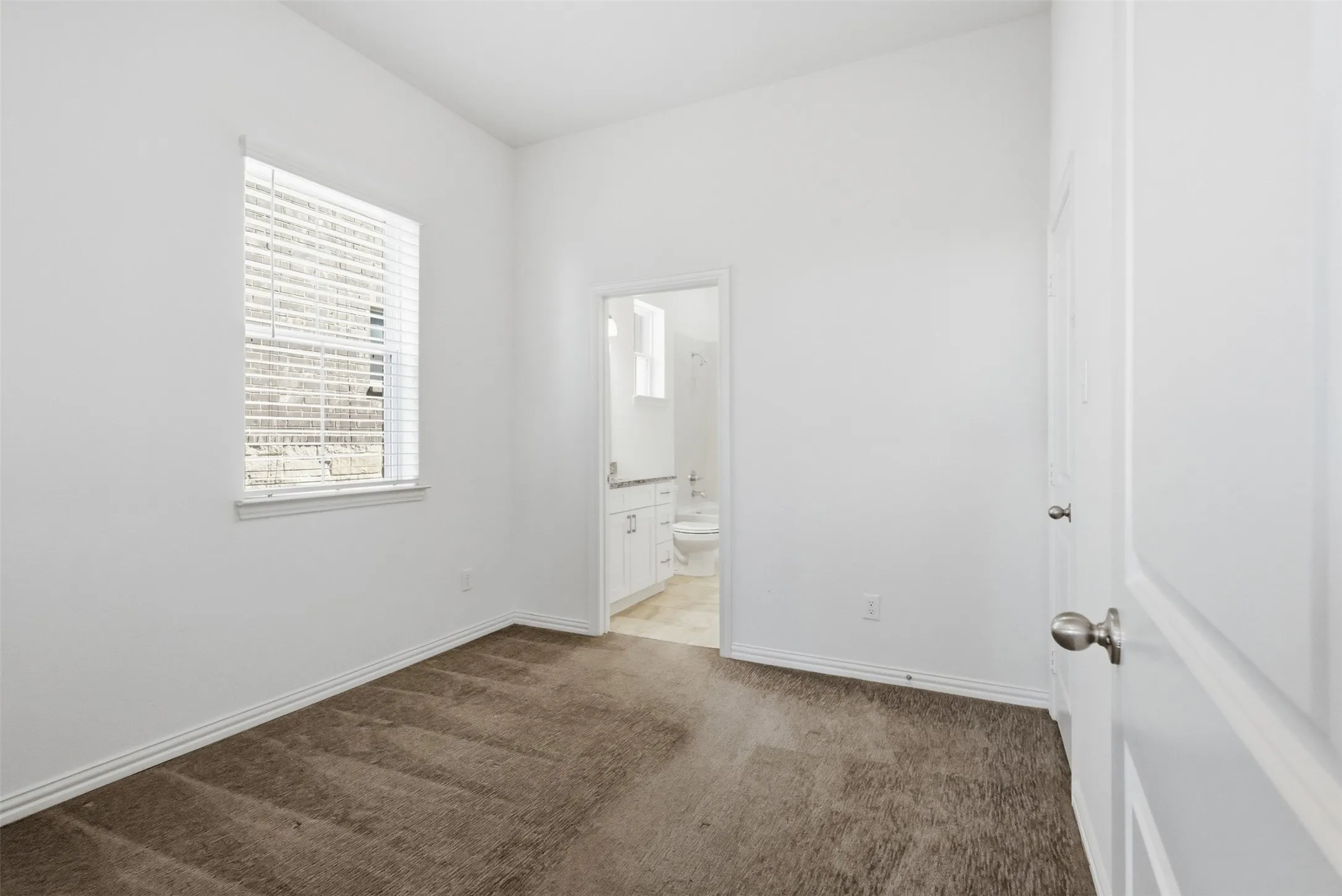 White walls, textured carpeting, and a window with blinds