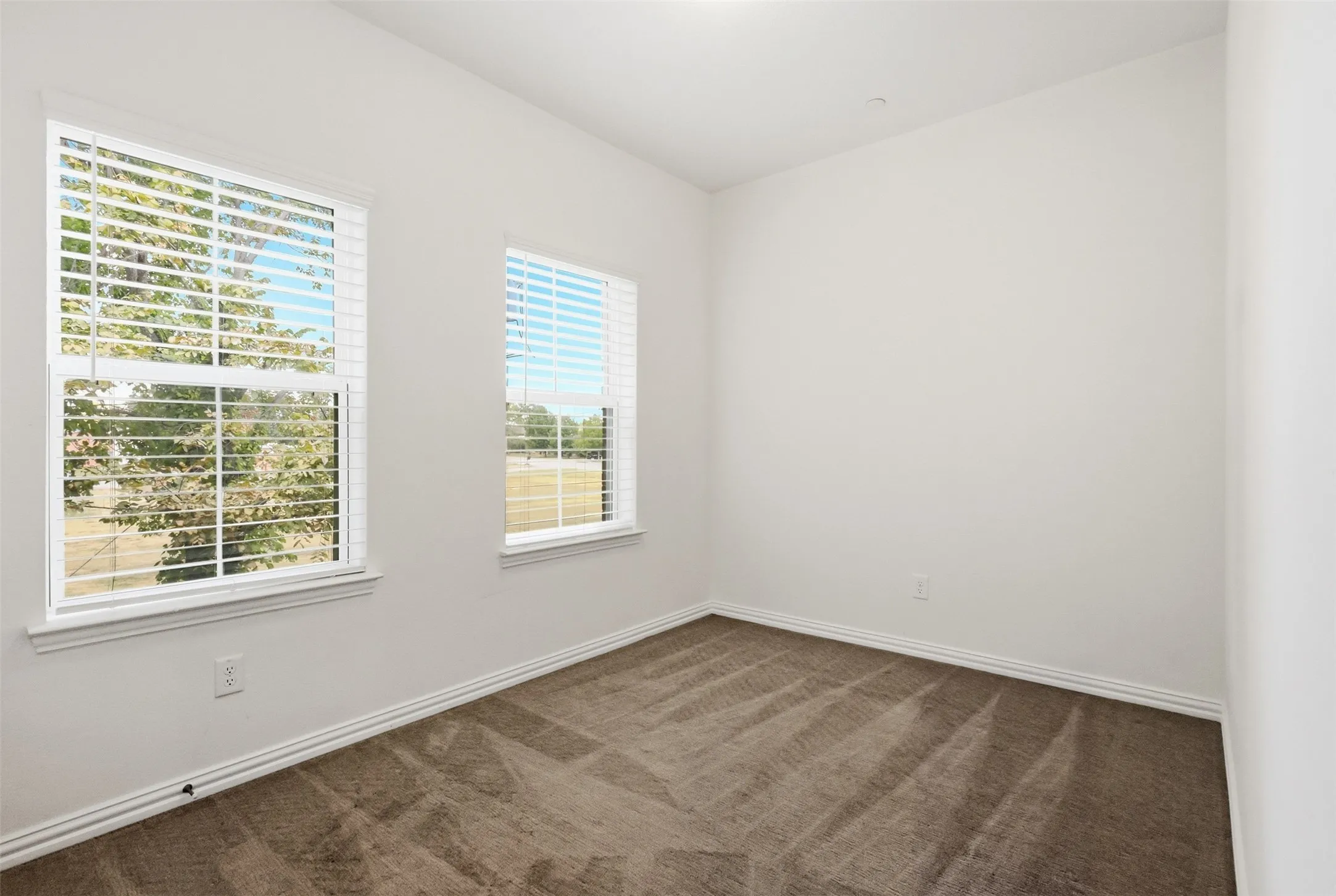 Two windows with white blinds, white trim, light-colored walls, and patterned carpet
