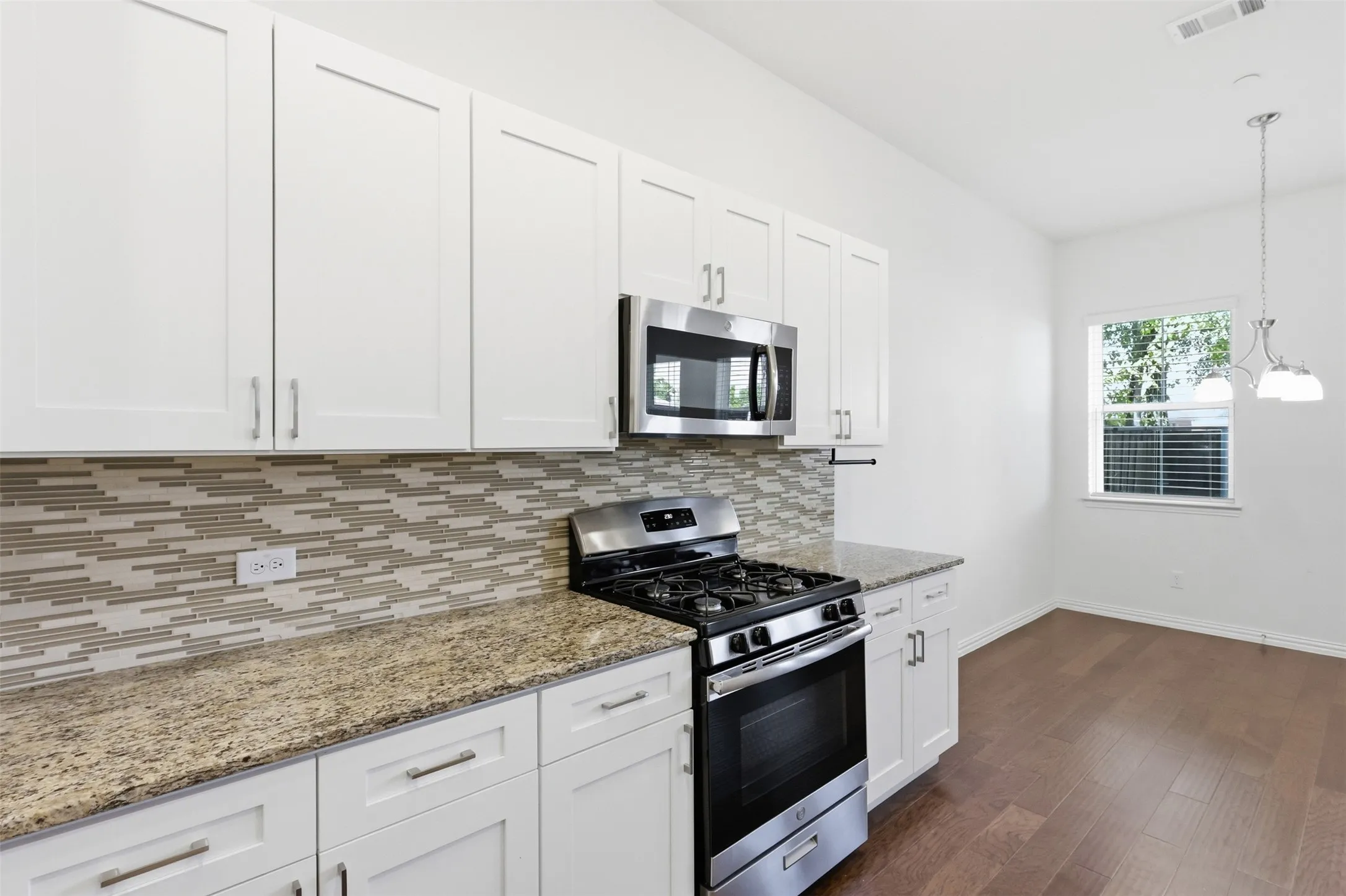 White shaker cabinetry, stainless steel appliances, granite countertops, decorative tile backsplash, and wood-finish flooring
