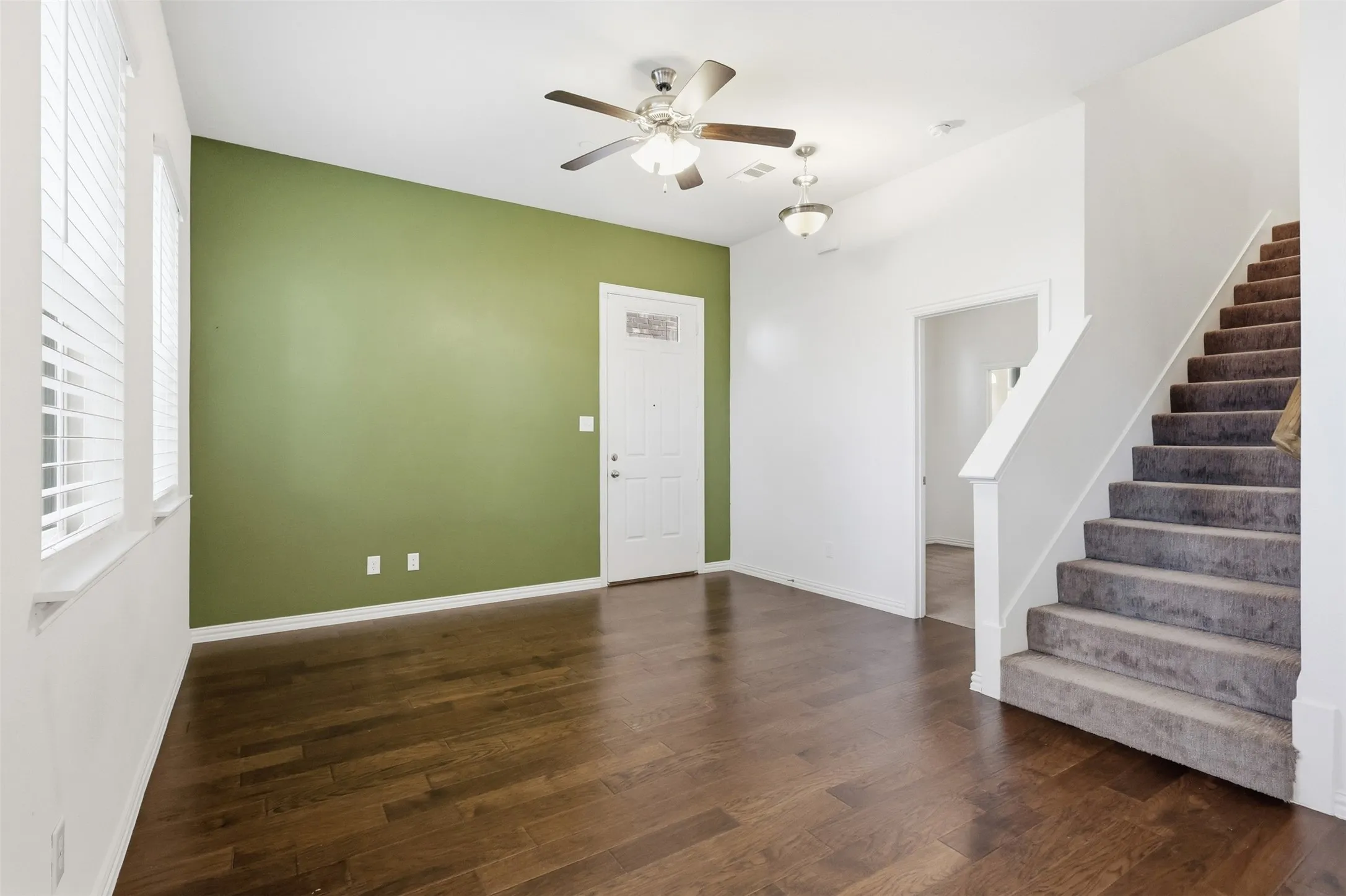Wood-finish flooring, staircase with carpeted treads, ceiling fans, and natural light from horizontal blinds