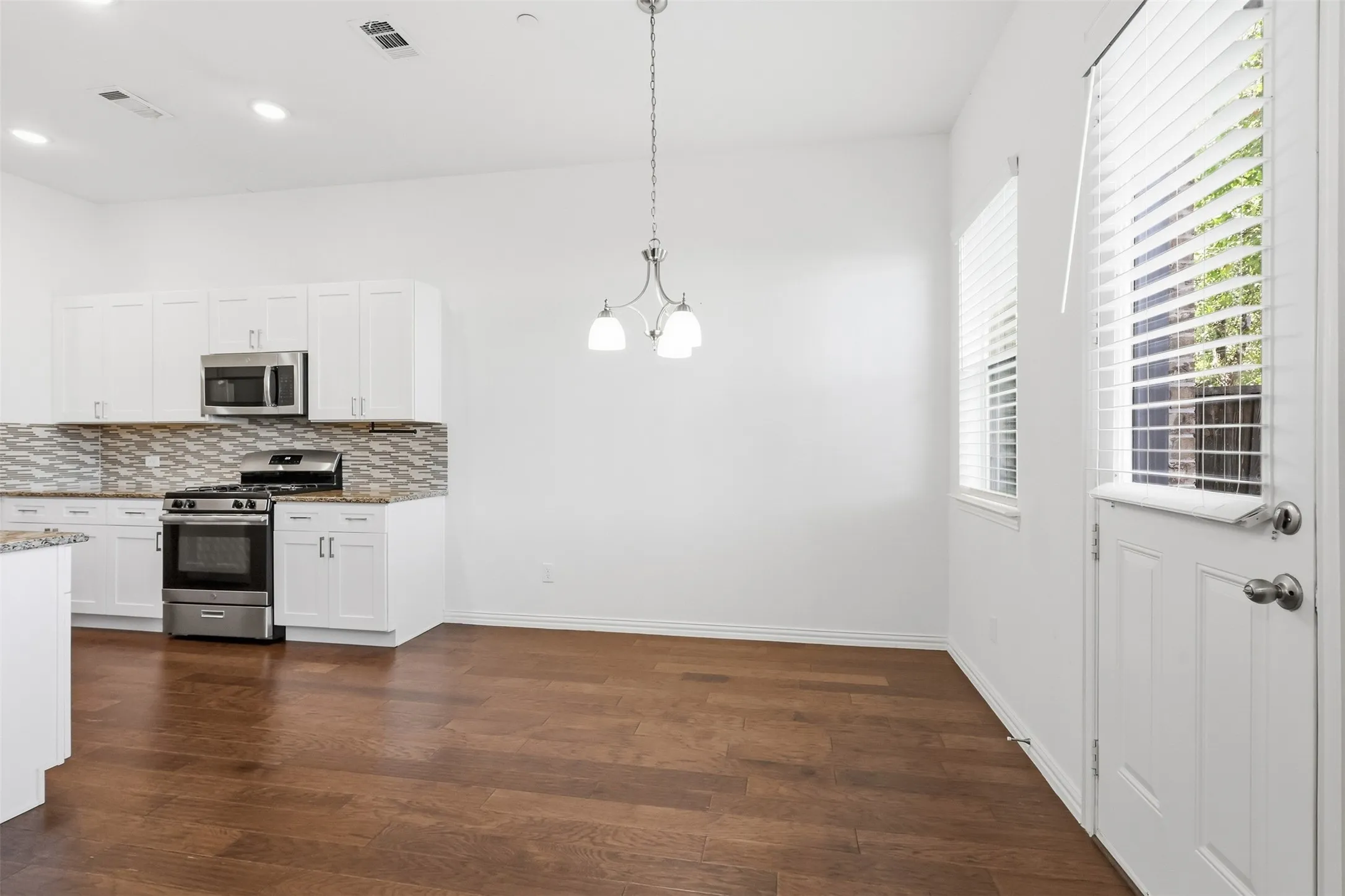 Wood-finish flooring, white cabinetry, stainless steel range, stainless steel microwave, and a decorative pendant light fixture
