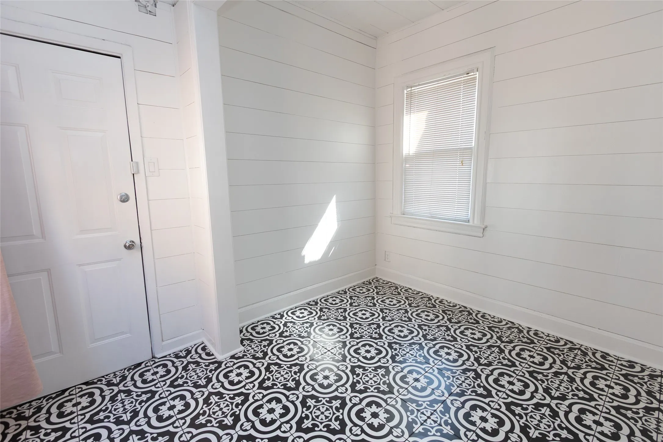 Patterned tile flooring, shiplap wall paneling, white paneled door, and window with blinds