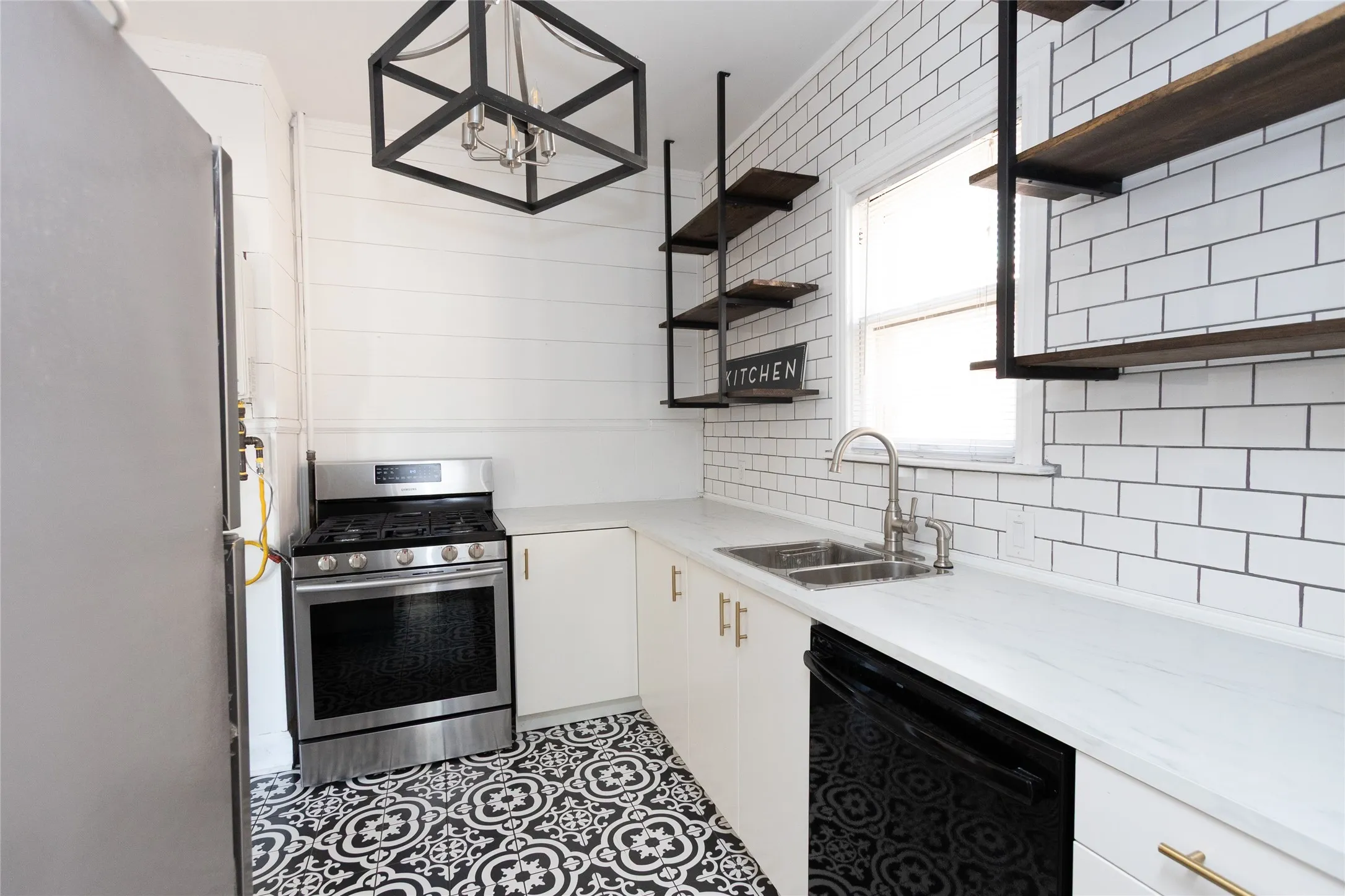 Patterned floor tiling, white subway tile backsplash, white countertops, built-in stainless steel gas range, and a dual basin sink with a gooseneck faucet