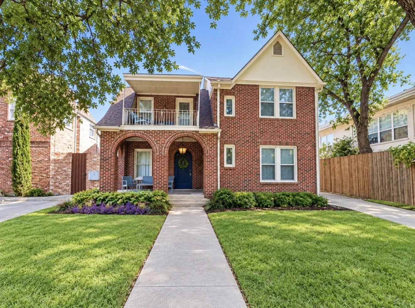 Brick exterior with a gabled roofline, arched entry, second-story balcony, and front lawn with mature trees