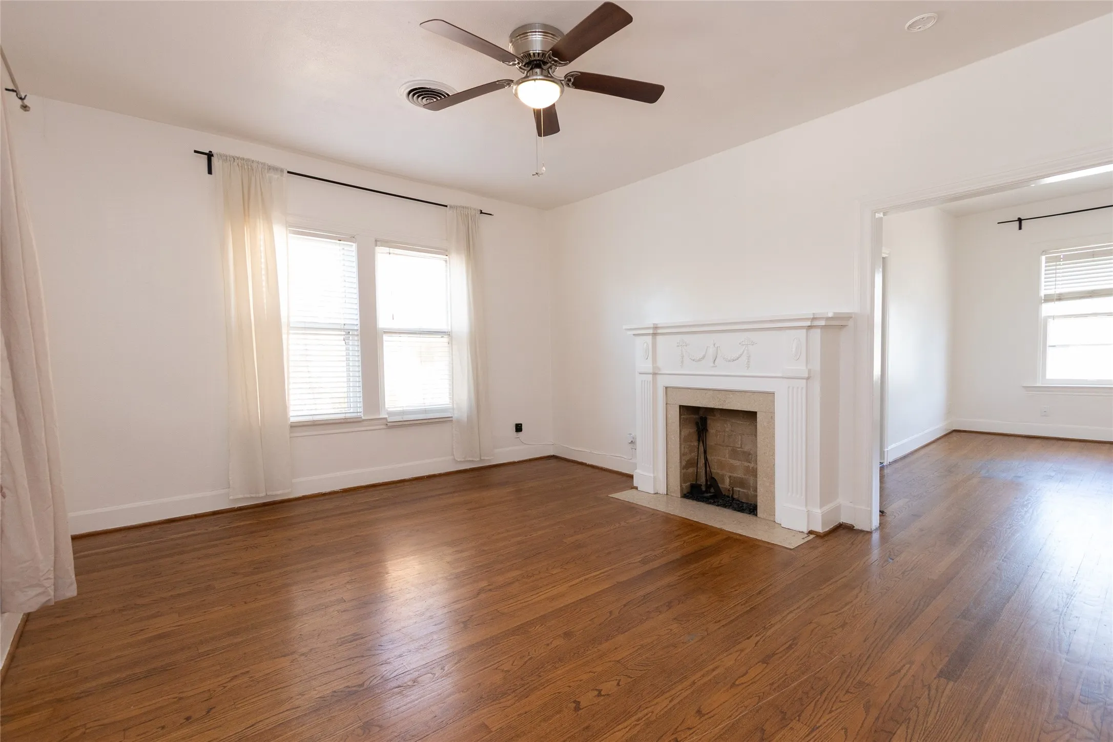 Expansive room featuring wood-finish flooring, a decorative fireplace with a stone surround, and multiple windows