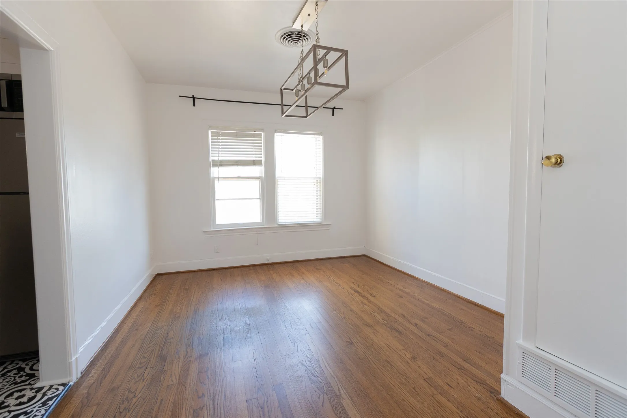 Hardwood-finish flooring, white painted walls, crisp white trim, dual windows with blinds, and a contemporary linear chandelier