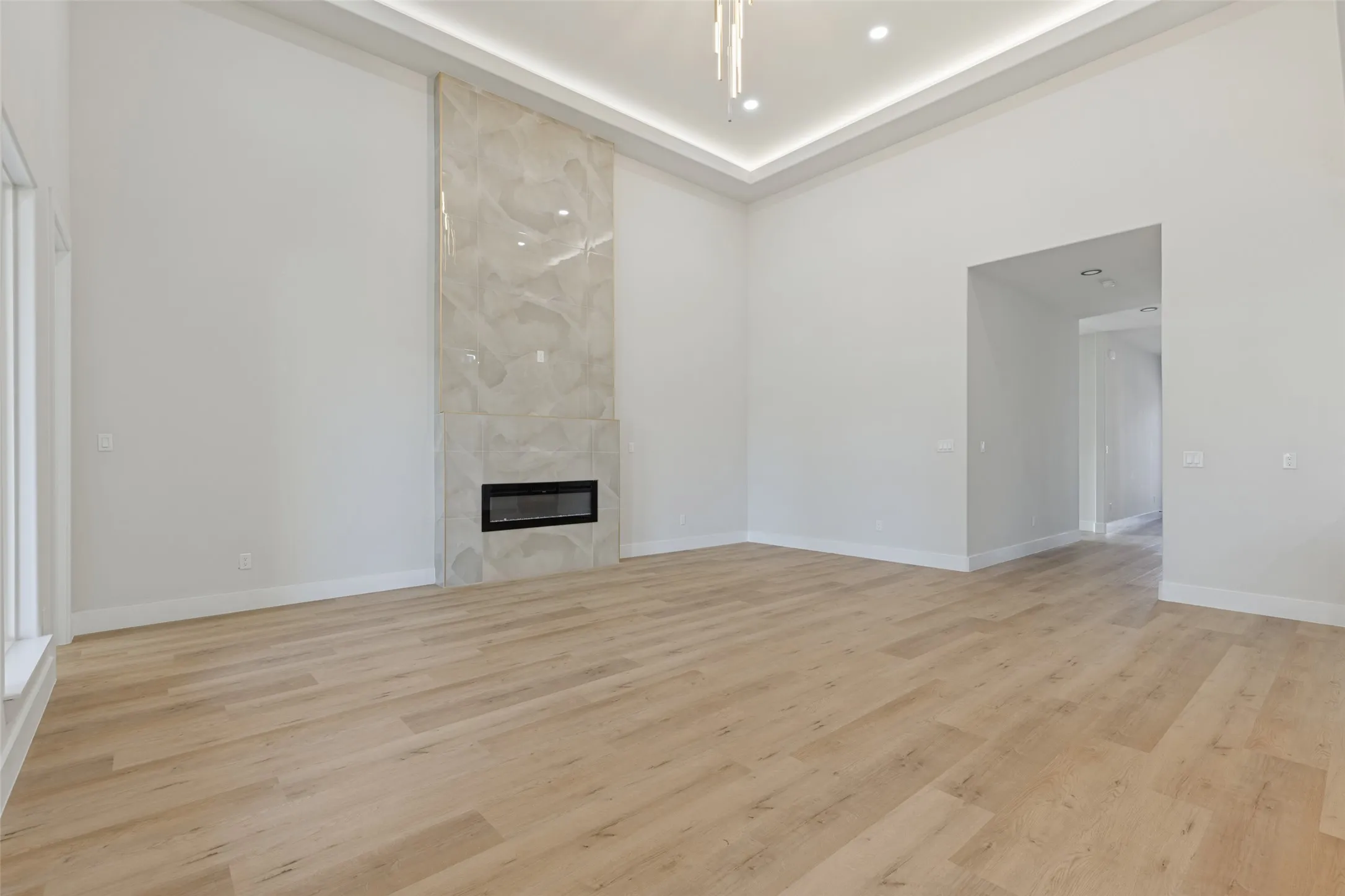 Spacious room featuring wood-finish flooring, a tall fireplace with a natural stone surround, recessed lighting, and a tray ceiling with integrated lighting