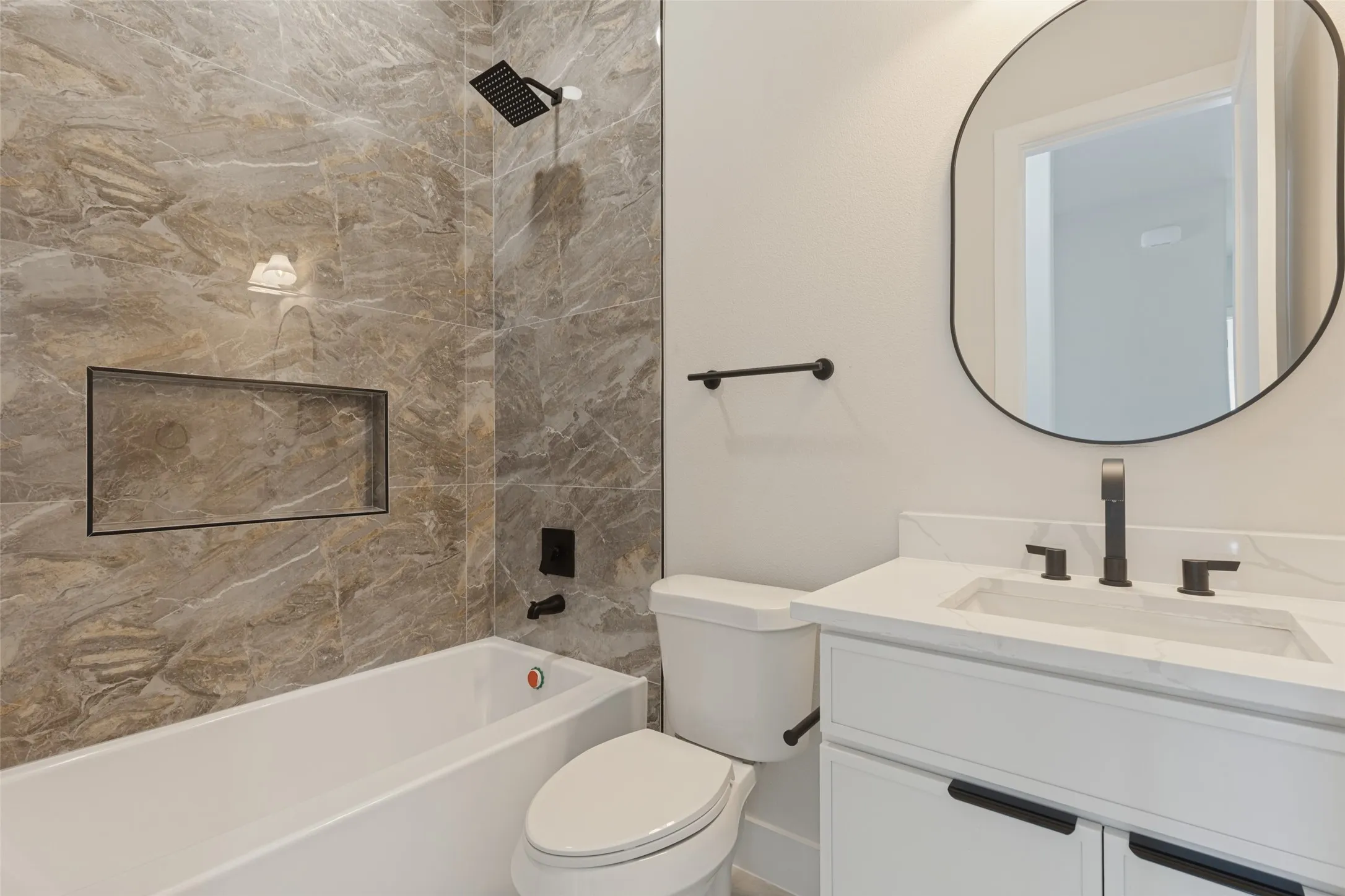 Tiled shower surround with an integrated niche, a white bathtub, a toilet, a vanity with a white countertop and undermount sink, and a framed mirror