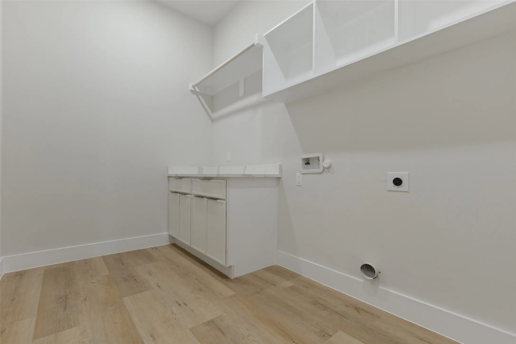 Wood-finish flooring with white baseboards, white cabinetry, and white wall shelving