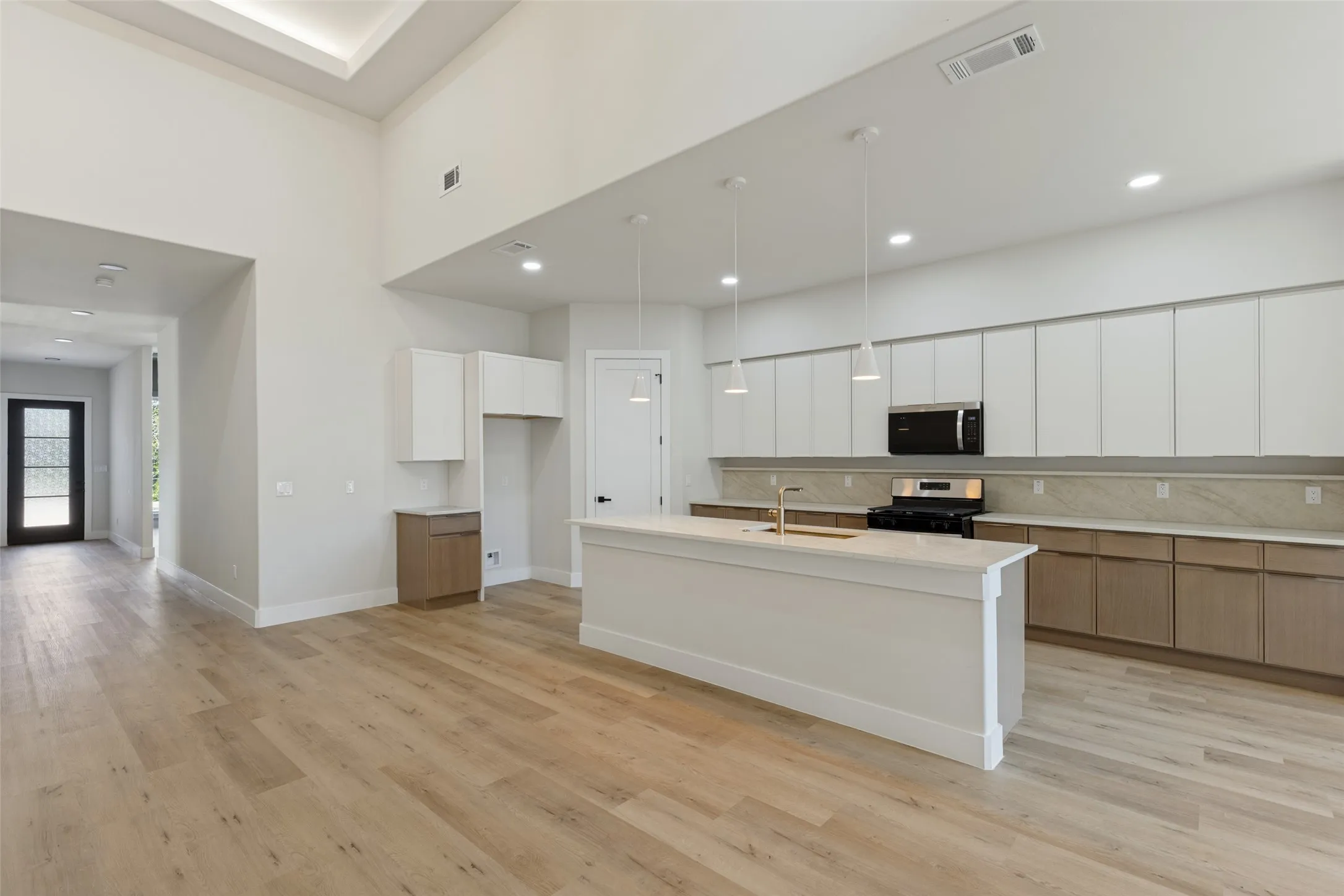 Soaring ceilings with recessed lighting, wood-finish flooring, a kitchen island with sink, stainless steel appliances, and two-tone cabinetry