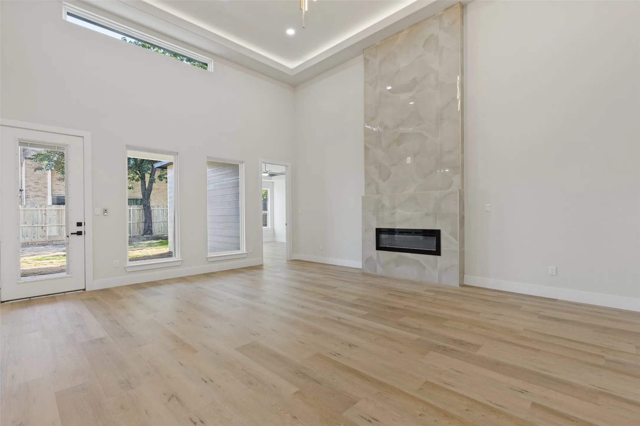 Soaring ceiling with a tray detail, wood-finish flooring, and a modern linear fireplace with a floor-to-ceiling surround