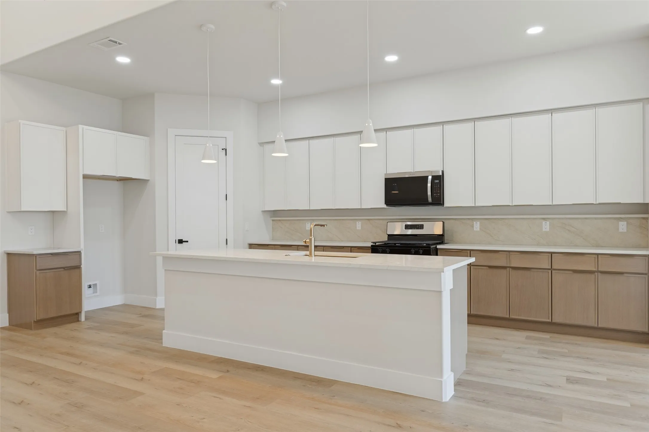 Spacious kitchen featuring an expansive island, light wood-finish flooring, two-tone cabinetry, stainless steel appliances, and pendant lighting