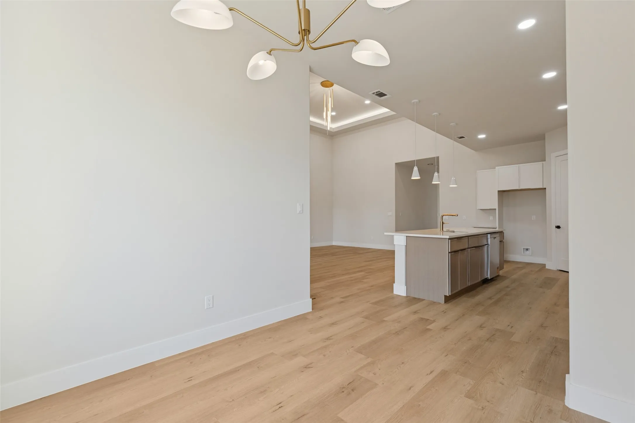 Wood-finish flooring, recessed lighting, kitchen island with sink and pendant lighting, white cabinetry, and tray ceiling with accent lighting