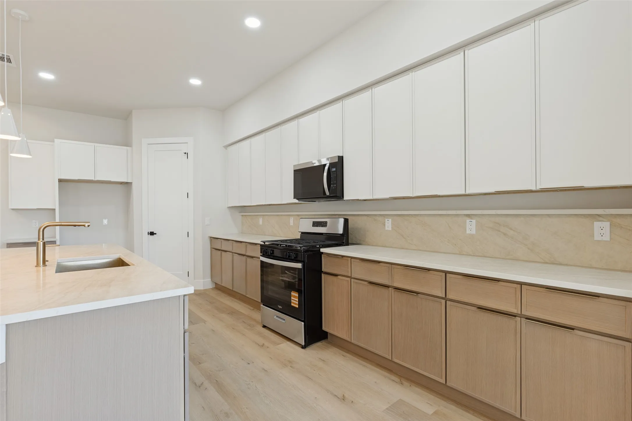 Kitchen featuring an undermount sink with a gold-finish faucet, recessed lighting, wood-finish flooring, two-tone cabinetry, and built-in appliances
