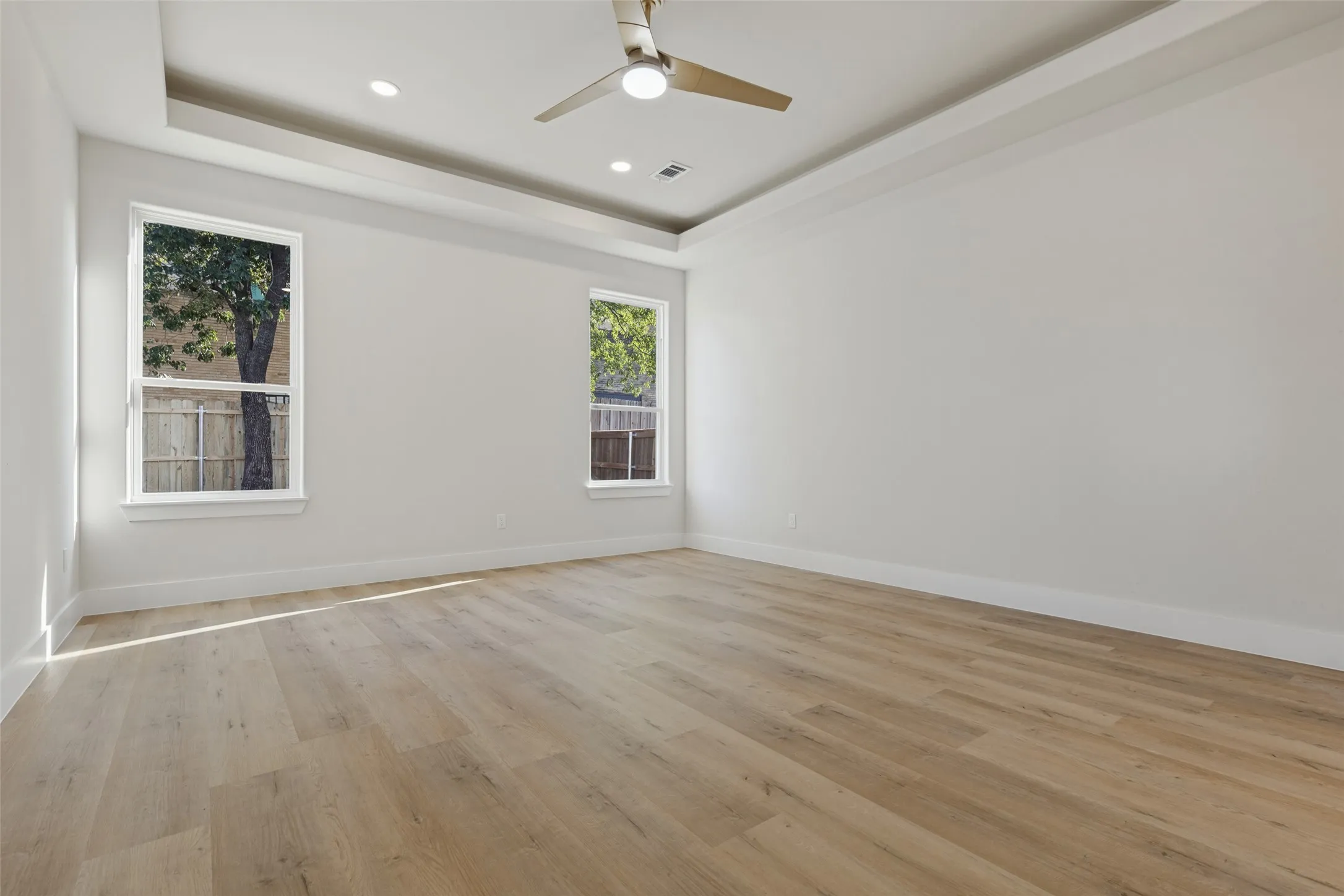 Tray ceiling with recessed lighting, ceiling fan, wood-finish flooring, and white window frames