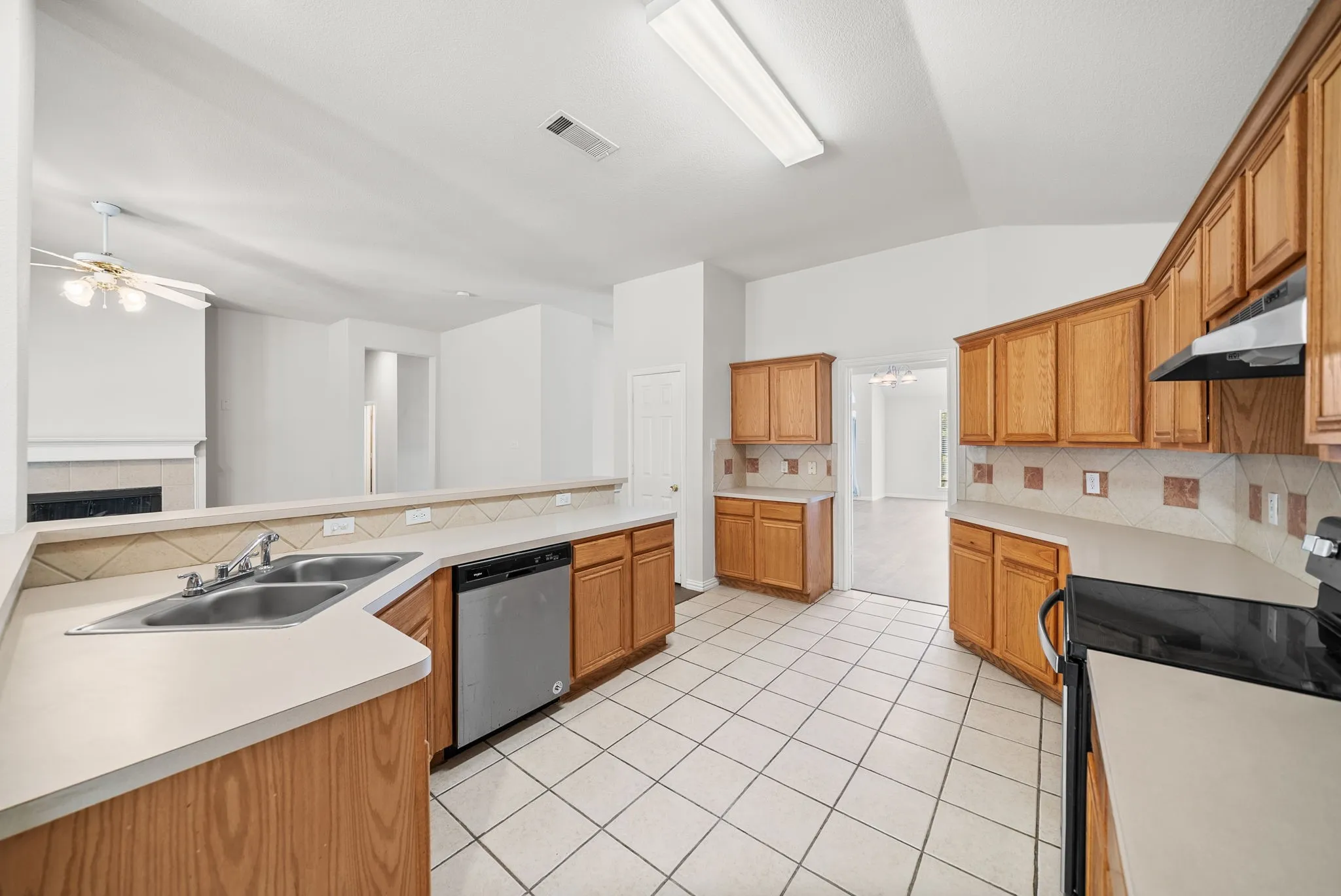 Kitchen featuring wood cabinetry, light-toned countertops, a stainless steel dishwasher, and tile flooring