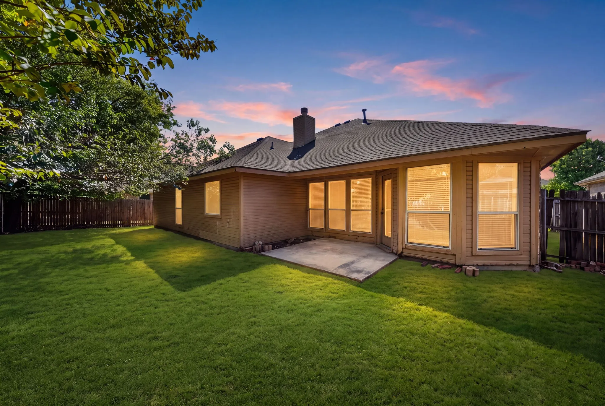 Expansive grassy yard with mature trees, a private wood fence, and a concrete patio