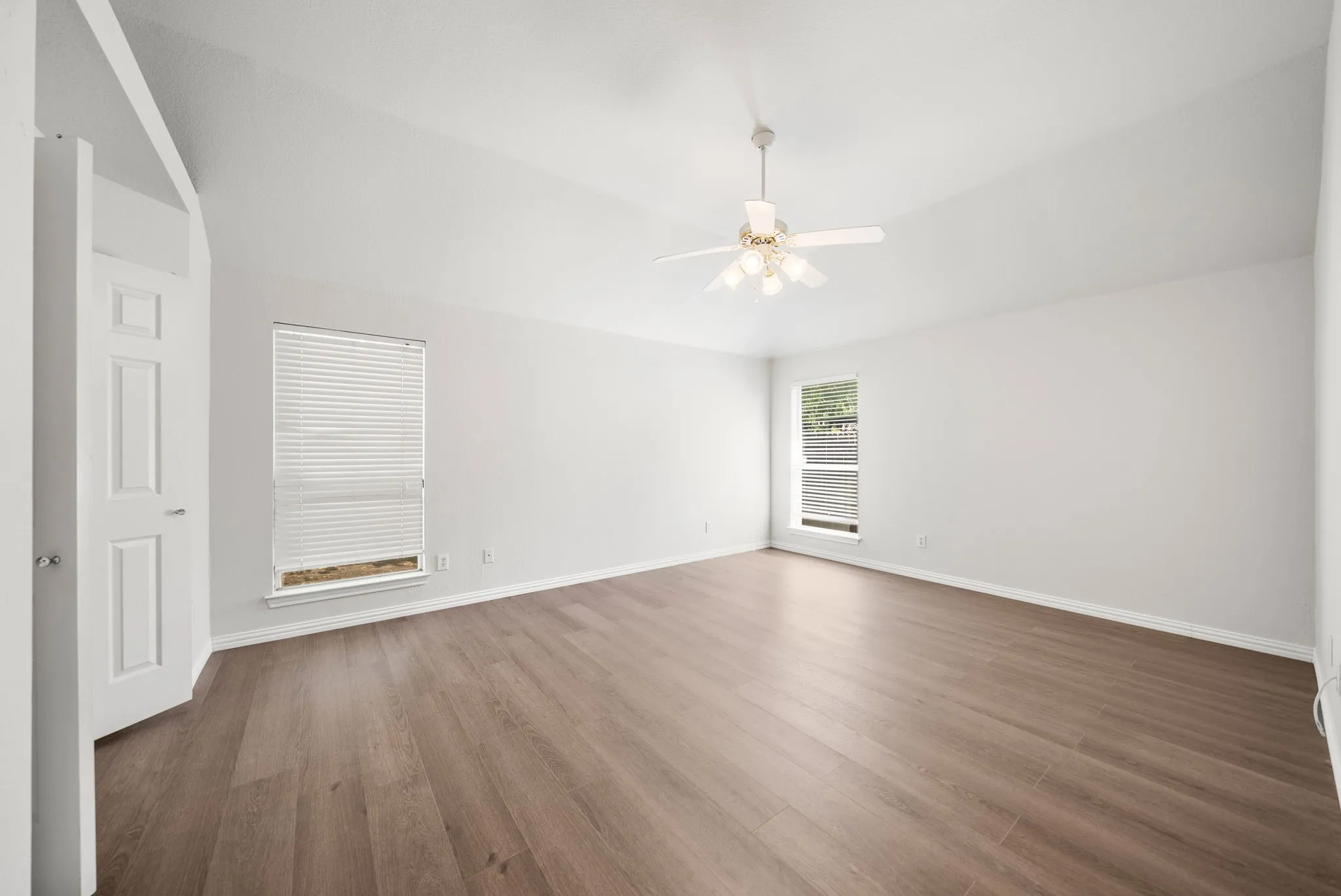 Vaulted ceiling featuring a ceiling fan with integrated lighting, wood-finish flooring, and white paneled doors