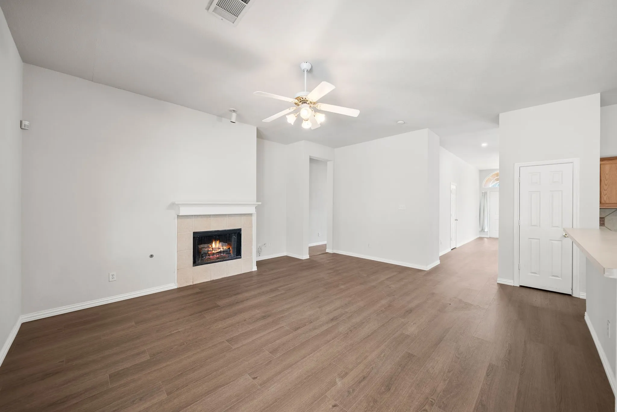 Spacious living area featuring a fireplace with a mantel, wood-finish flooring, a ceiling fan with integrated lighting, and neutral wall tones