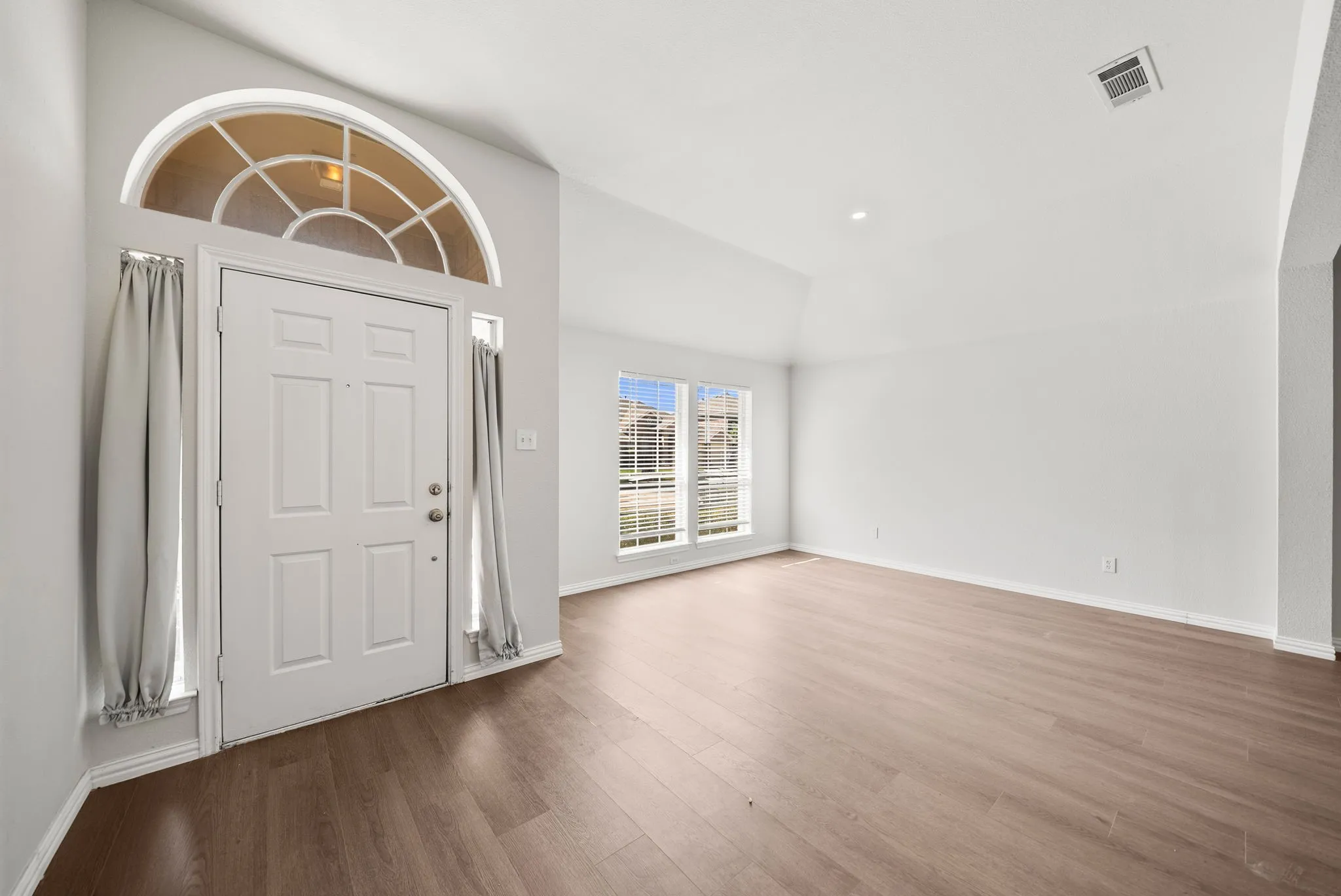 Entryway with a vaulted ceiling, wood-finish flooring, and a paneled front door with an arched transom window and sidelights
