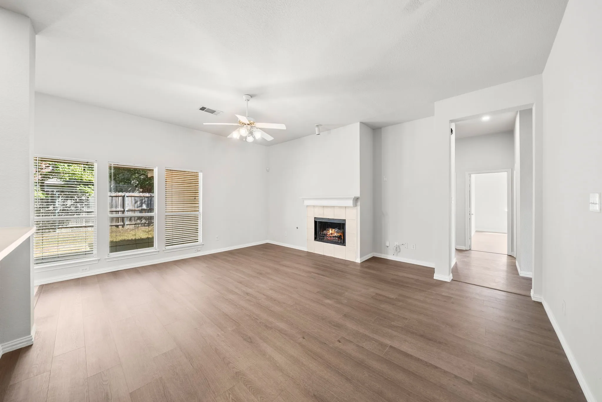 Vaulted ceiling with a ceiling fan, recessed fireplace with tile surround, wood-finish flooring, and multiple window openings