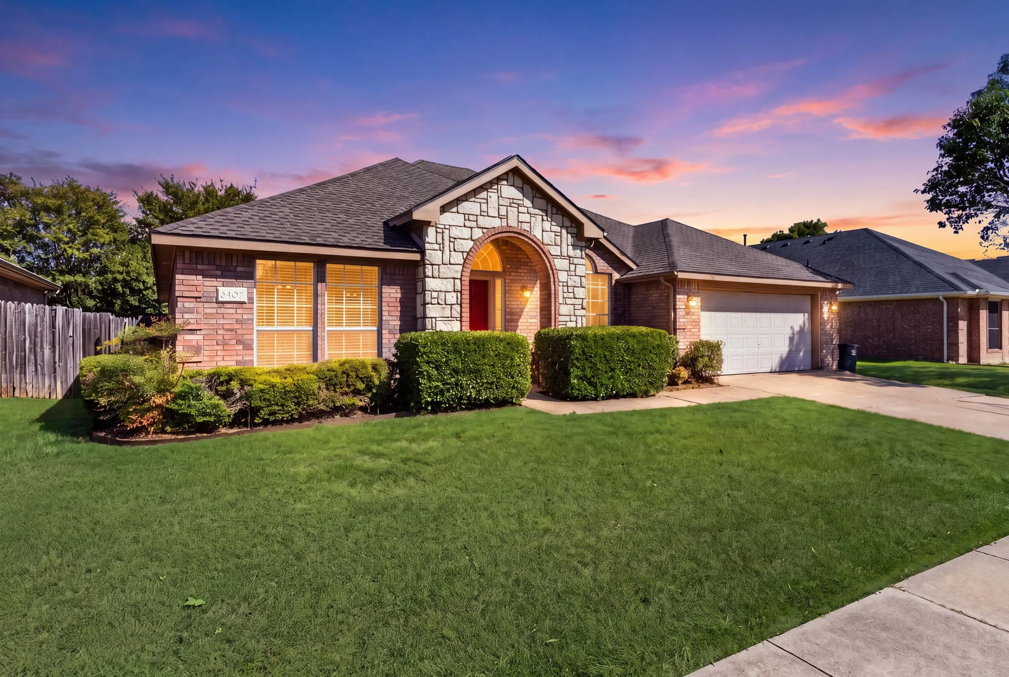 Brick exterior with stone accents, arched entryway, attached garage, and established landscaping