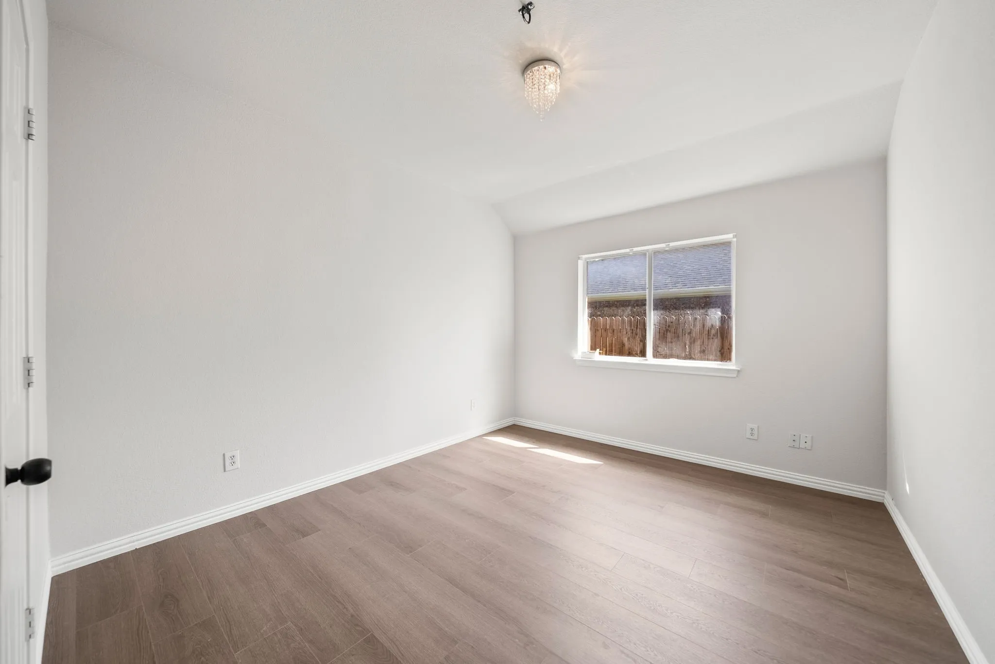 Neutral wall color, wood-finish flooring, single window, and a decorative ceiling light fixture
