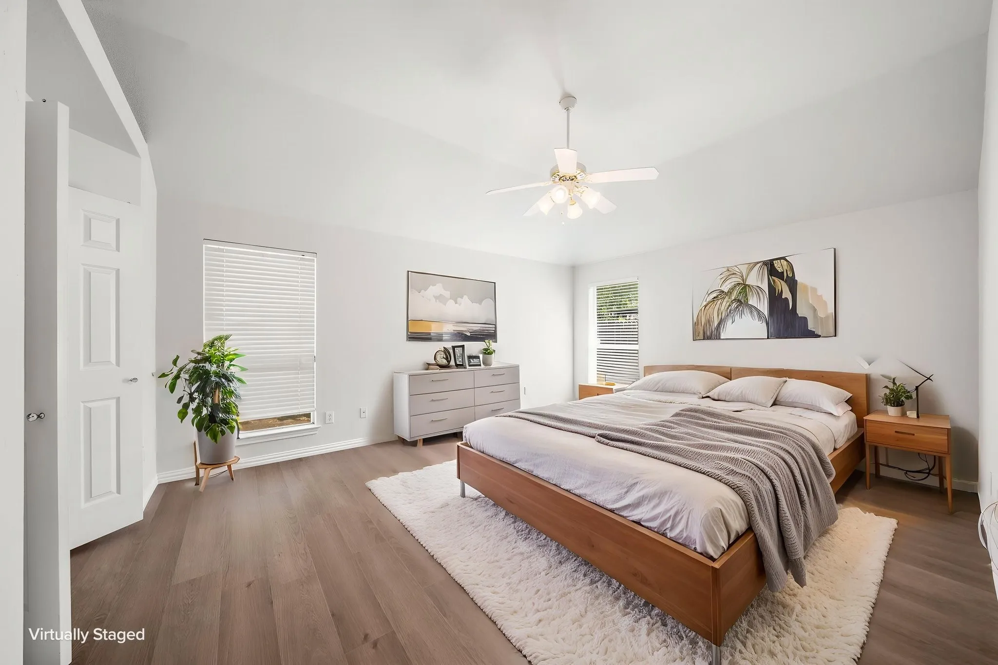 Vaulted ceilings, wood-finish flooring, white paneled door, and recessed windows with blinds
