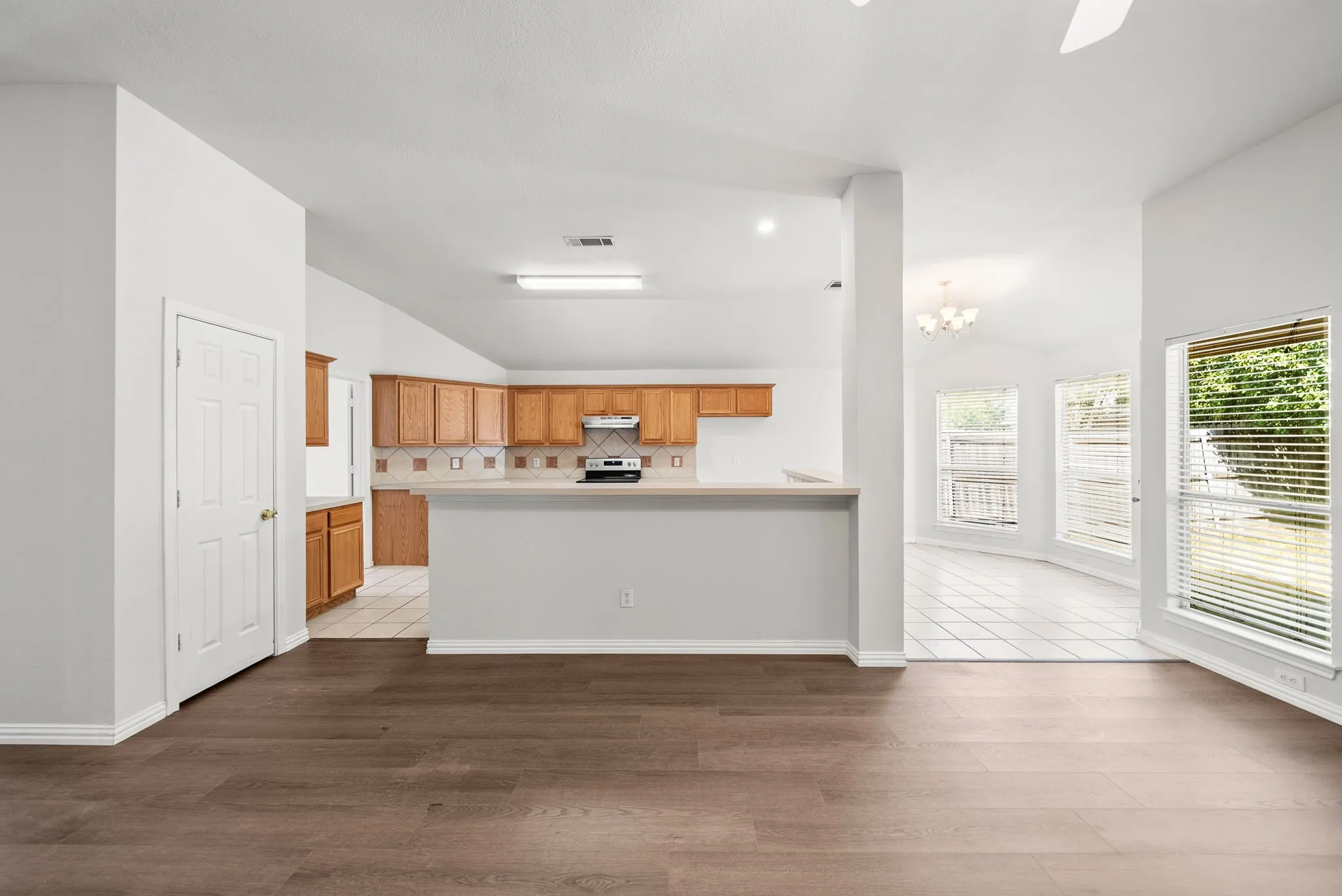 Wood-finish flooring, vaulted ceilings, kitchen with wood cabinetry and tile backsplash, breakfast bar, and multiple windows