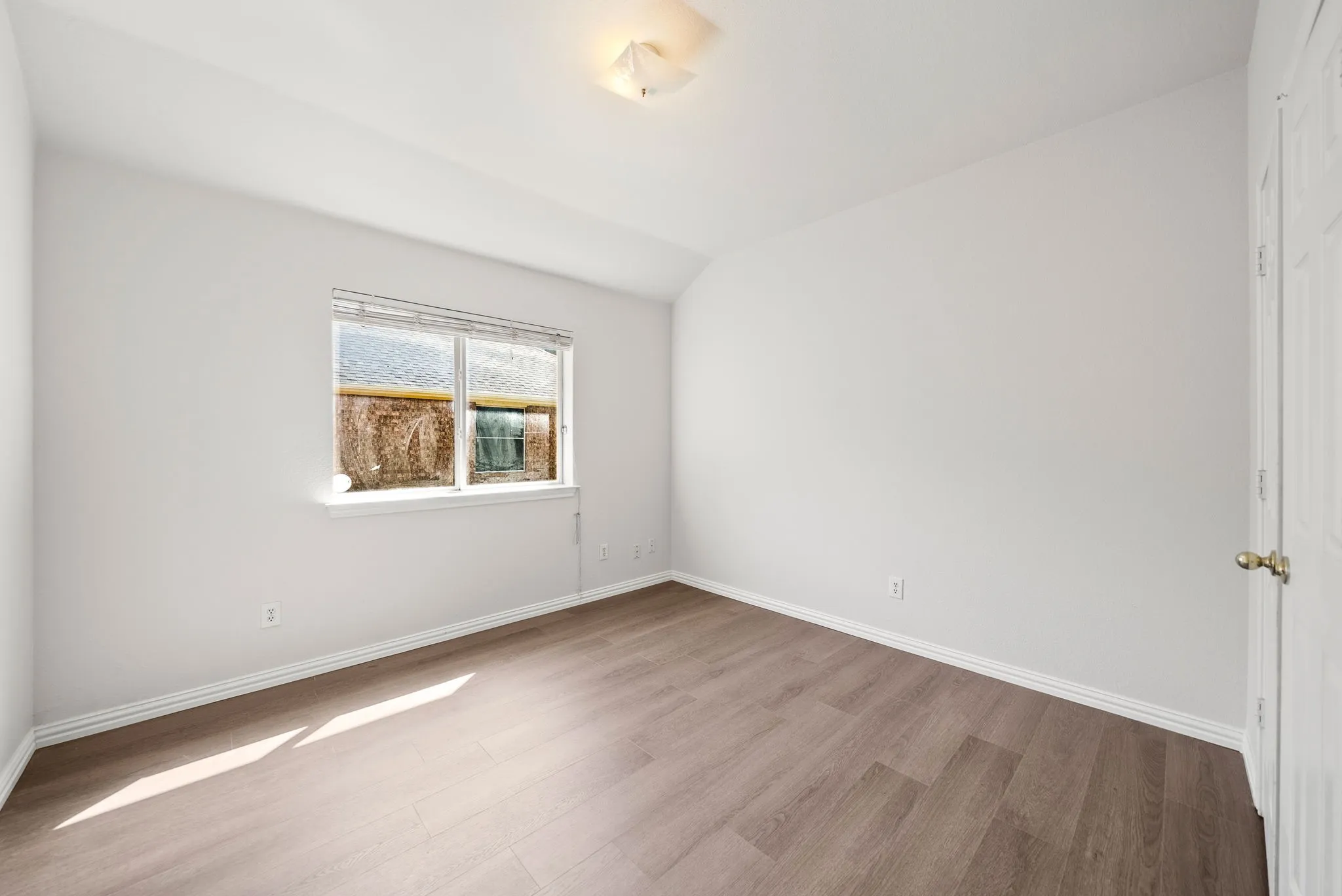 Wood-finish flooring, white walls, and a window with blinds