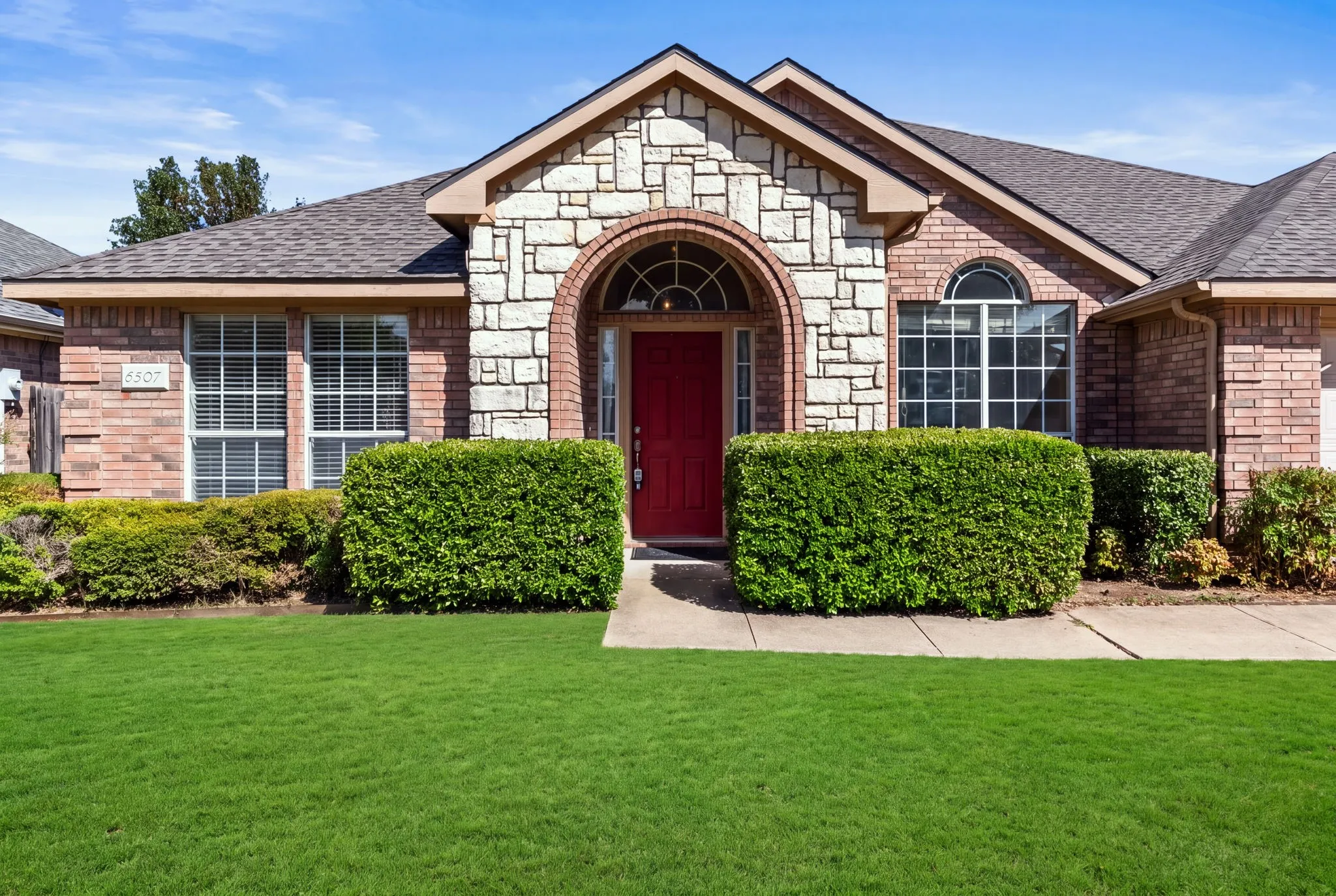 Brick and stone facade with an arched entryway, a vibrant red front door, and a well-maintained lawn