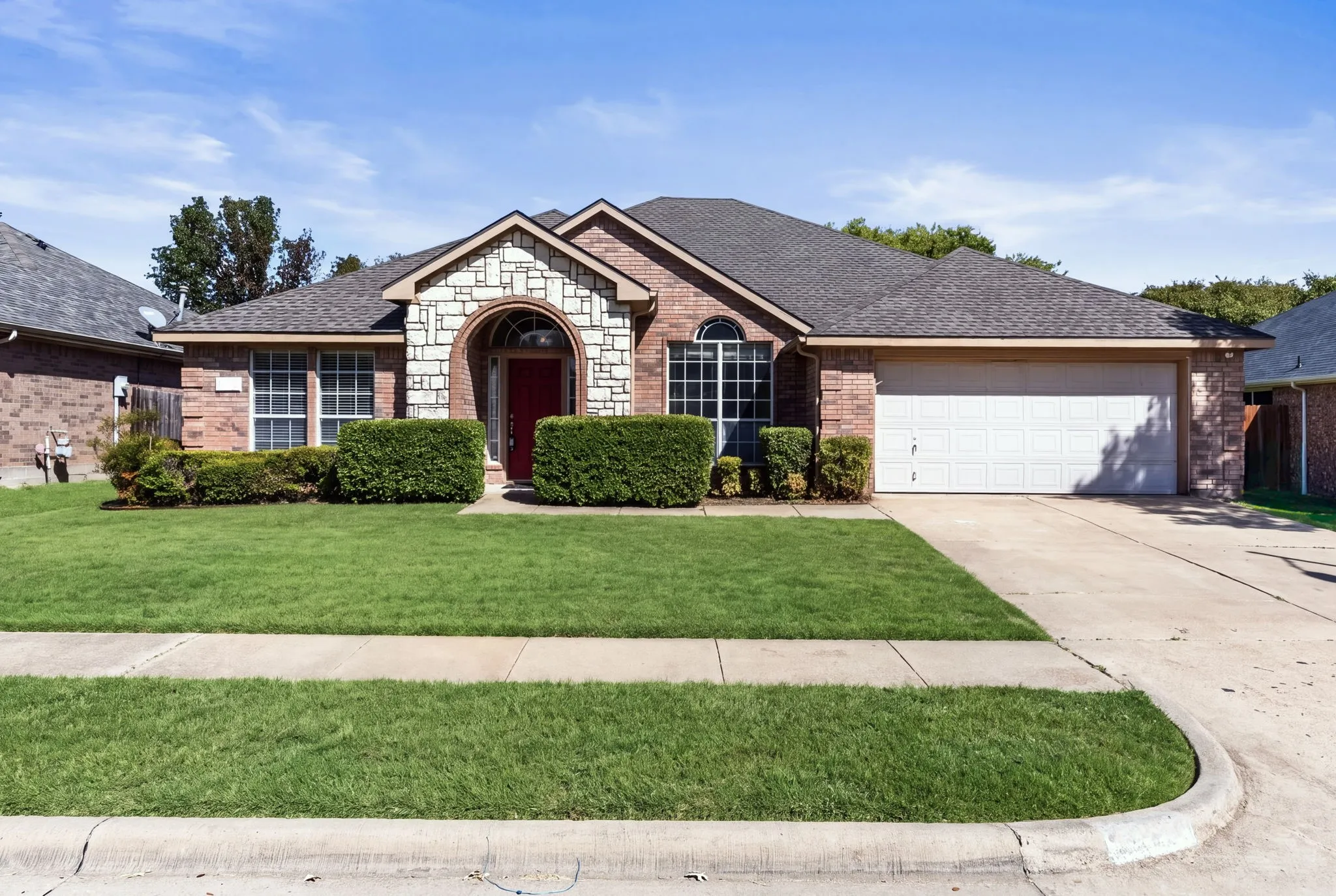 Brick exterior with stone accents, arched entryway, attached garage, concrete driveway, and manicured landscaping