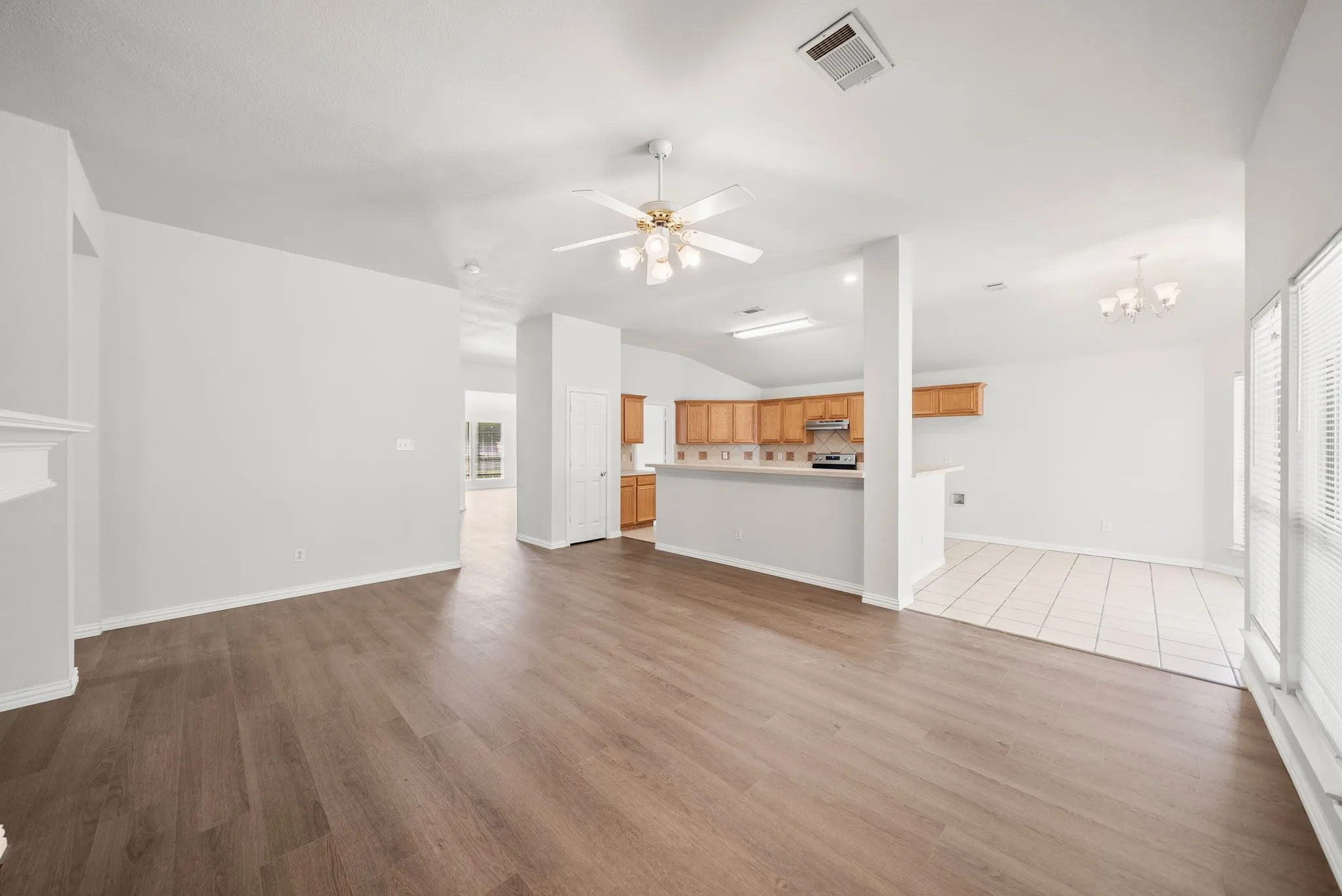 Vaulted ceiling with a ceiling fan, wood-finish flooring, kitchen with wood cabinetry, white tile flooring, and ample natural light from multiple windows