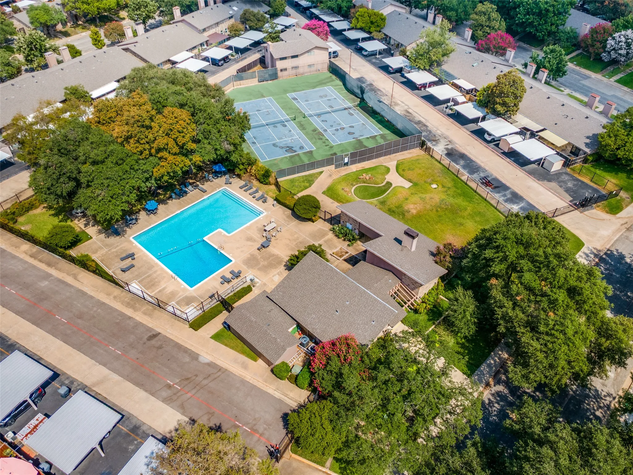Outdoor swimming pool with a concrete deck, two tennis courts, and a grass recreation area