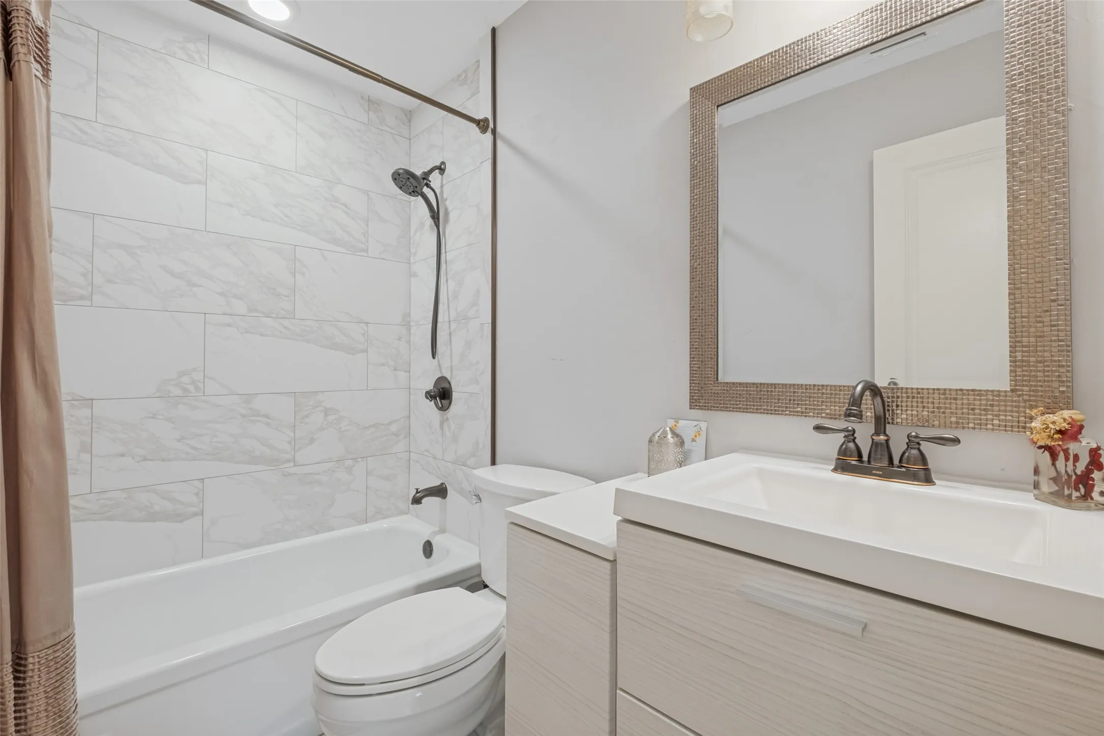 Bathtub with full-height tile surround, wall-mounted shower fixture, toilet, vanity with integrated sink, and framed mirror