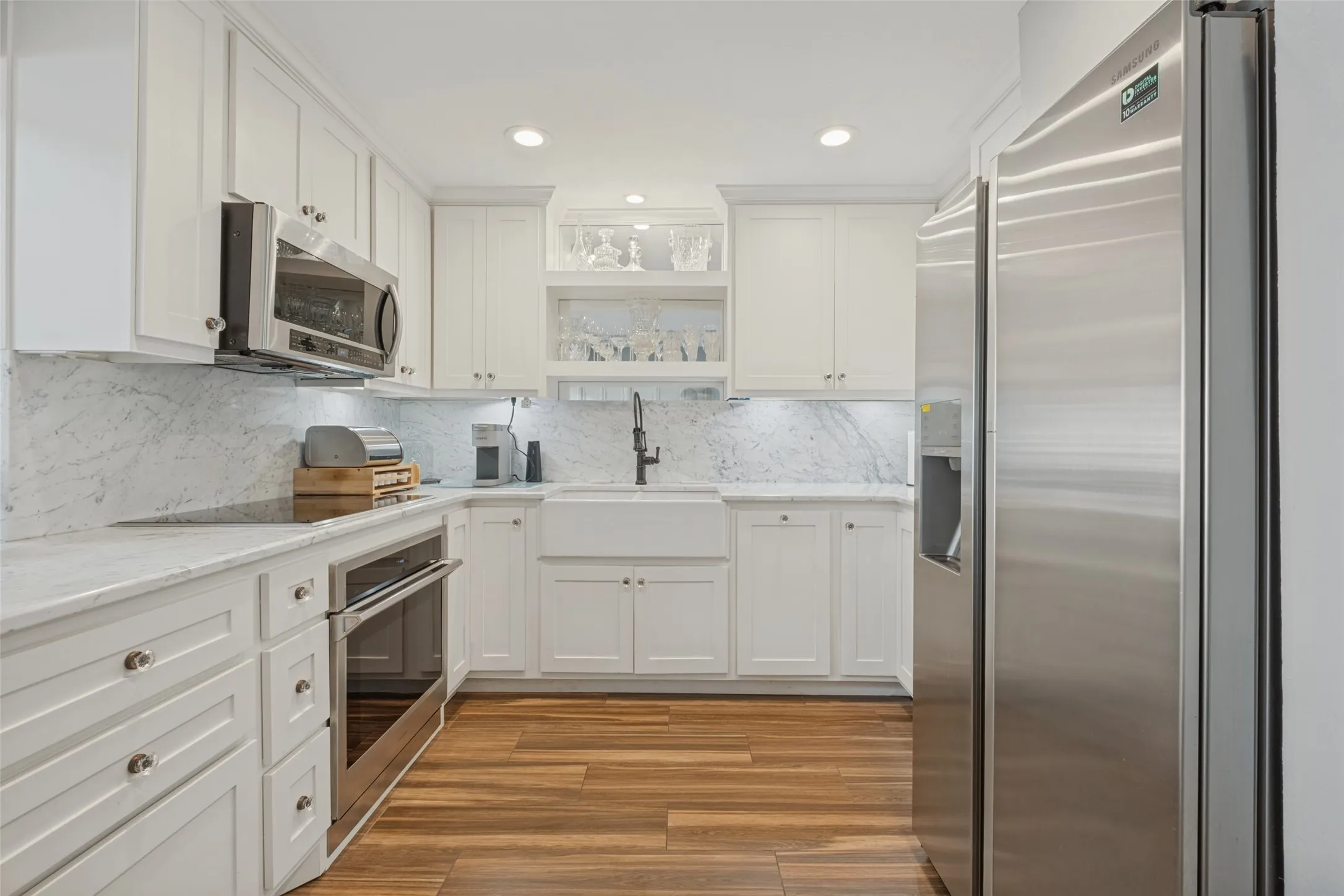 White shaker-style cabinetry, stainless steel appliances, wood-finish flooring, undermount sink, and recessed lighting
